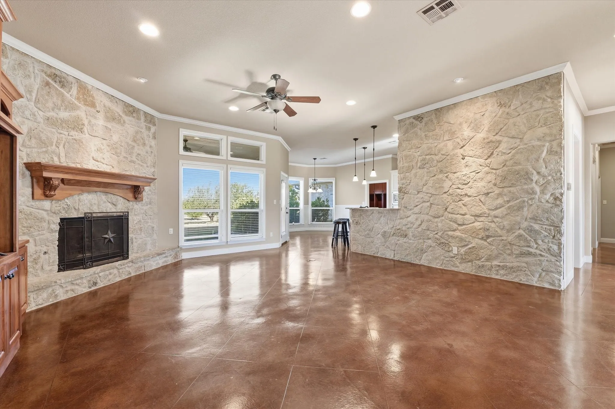 Spacious living area featuring polished concrete flooring, a stone-accented fireplace with a wood mantel, and multiple windows providing natural light