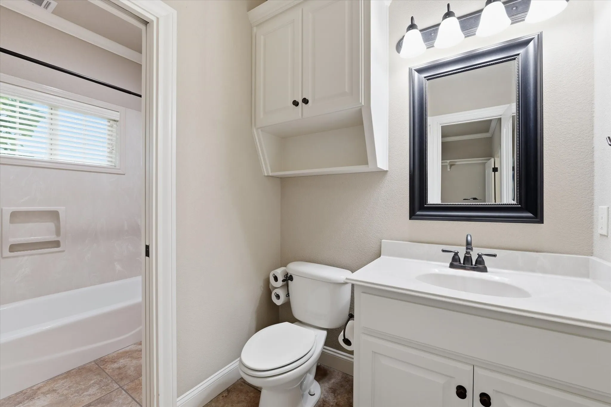Bathroom featuring a white vanity with a white countertop, framed mirror, and wall-mounted light fixture