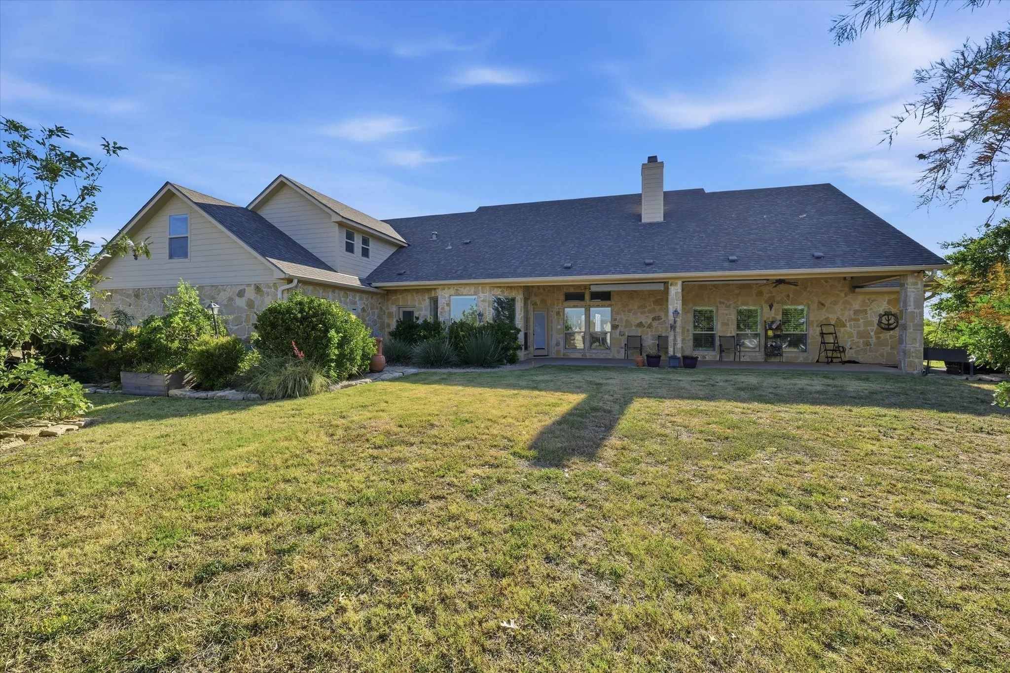 Stone exterior with a covered patio, multiple windows, and extensive lawn space