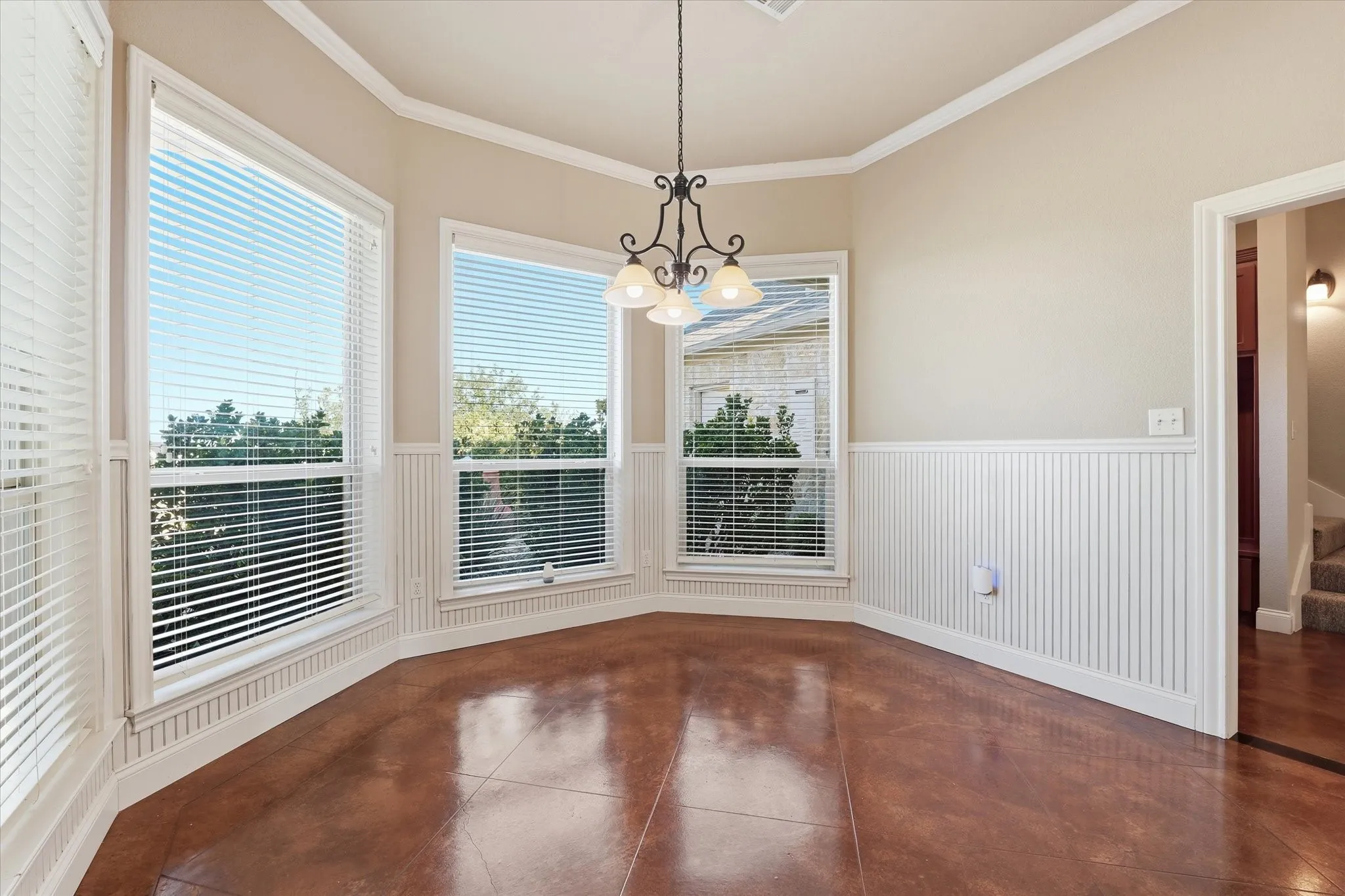 Bay window alcove featuring three large windows, beadboard wainscoting, crown molding, a decorative chandelier, and polished concrete flooring