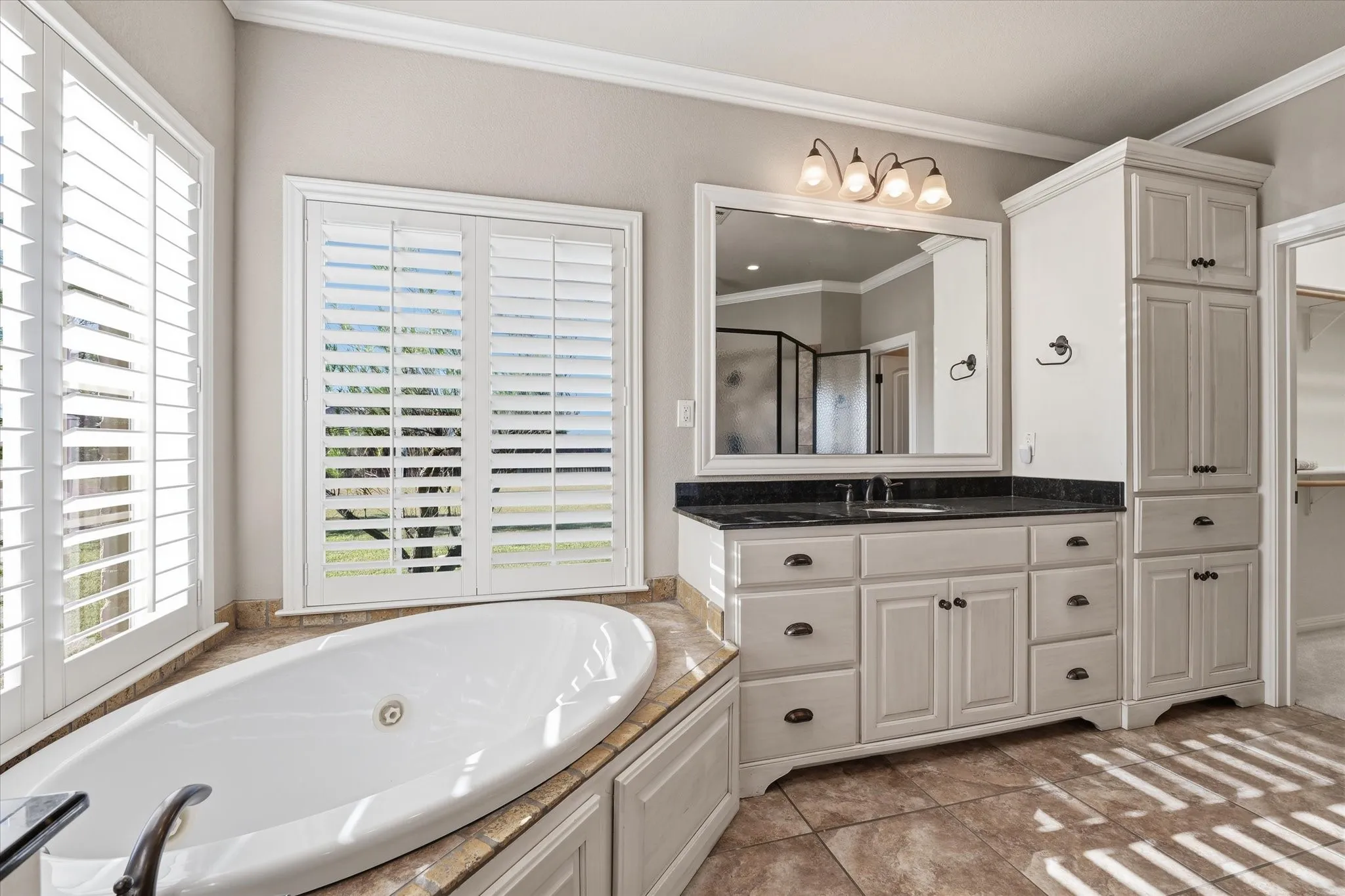 Bathroom featuring a freestanding soaking tub, dual windows with plantation shutters, a vanity with a dark countertop and undermount sink, and extensive built-in cabinetry