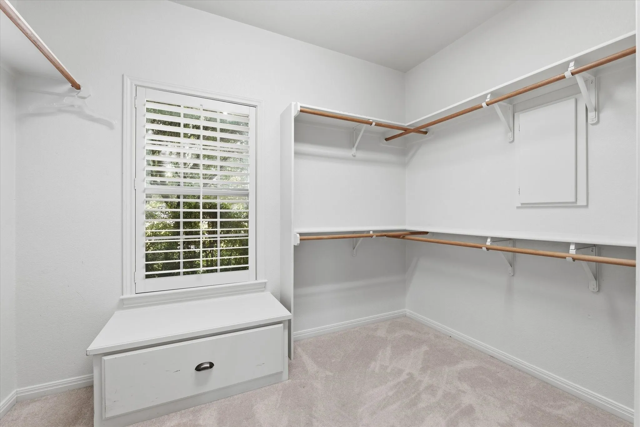 Walk-in closet featuring built-in shelving, wood-finish hanging rods, a window with plantation shutters, a window seat, and a built-in storage drawer