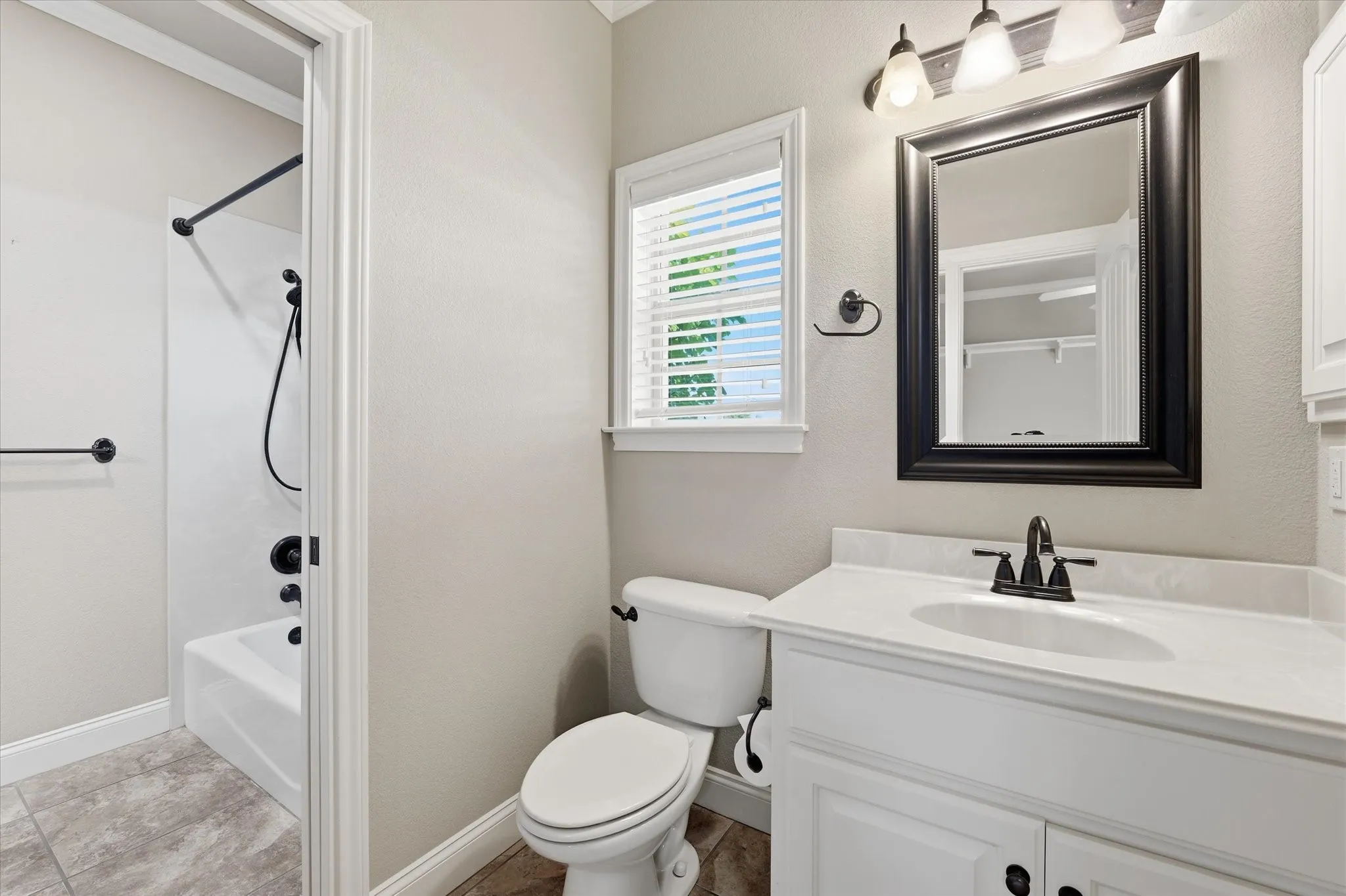 Bathroom featuring a white vanity with an integrated sink, dark bronze hardware, a framed mirror, and a full bathtub with a shower