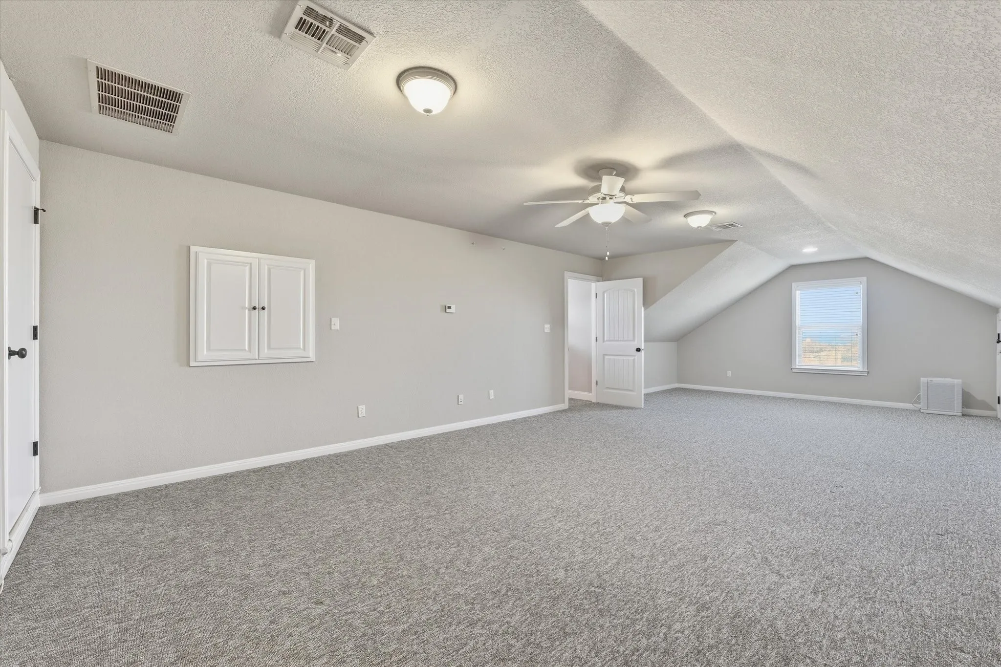 Spacious carpeted room featuring a ceiling fan, recessed lighting, built-in wall cabinet, and a window