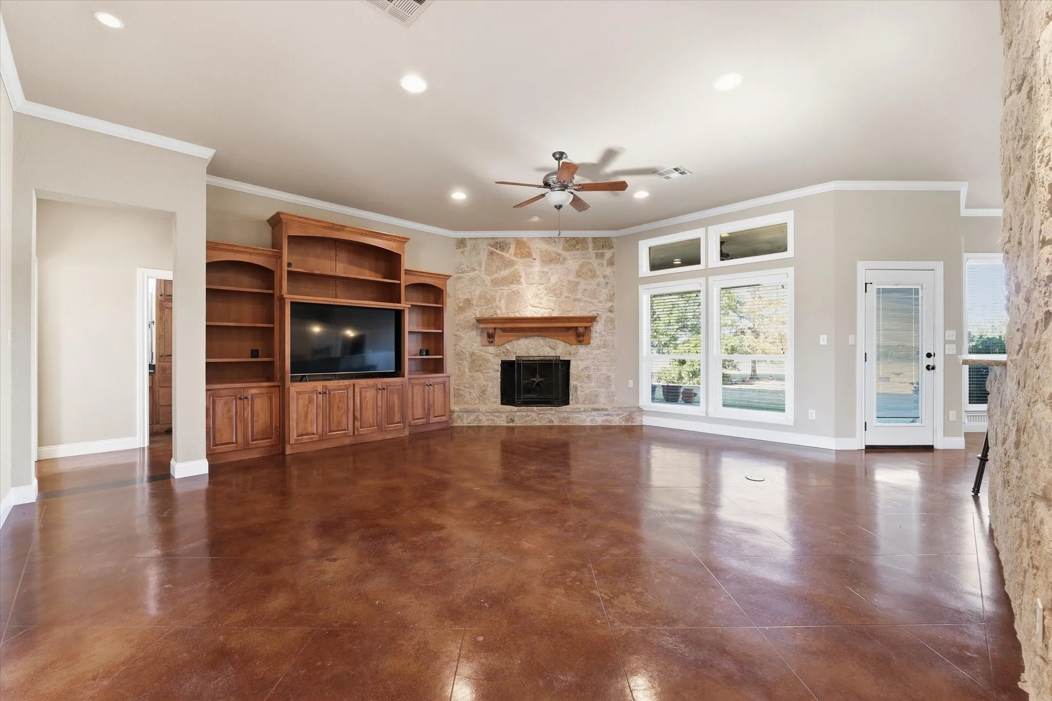 Spacious living area featuring brown concrete flooring, a natural stone fireplace with a wood mantel, and built-in wood cabinetry