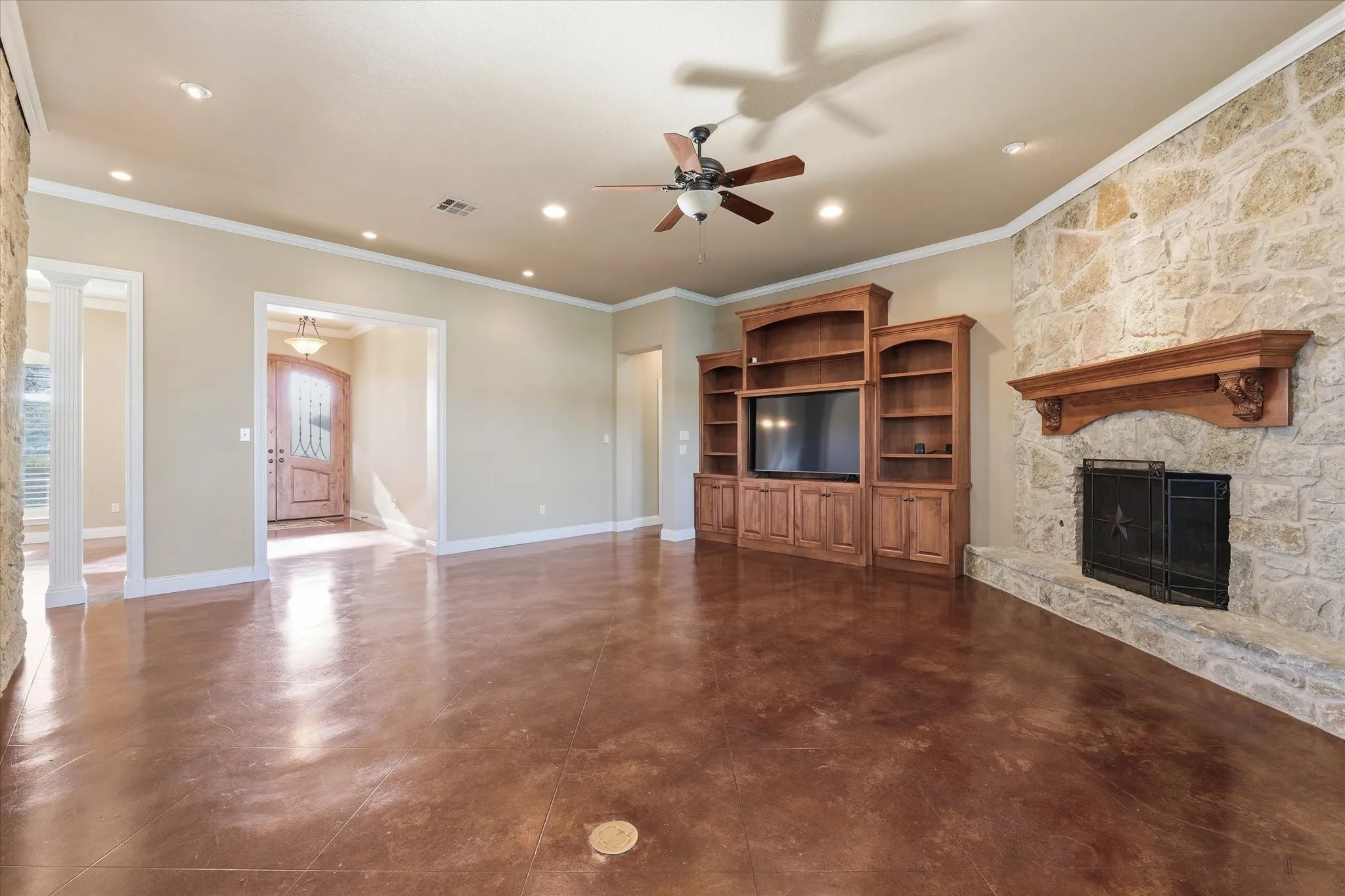 Living area featuring rich copper-toned concrete flooring, a stone accent wall with a large fireplace, a custom built-in entertainment center, recessed lighting, and crown molding