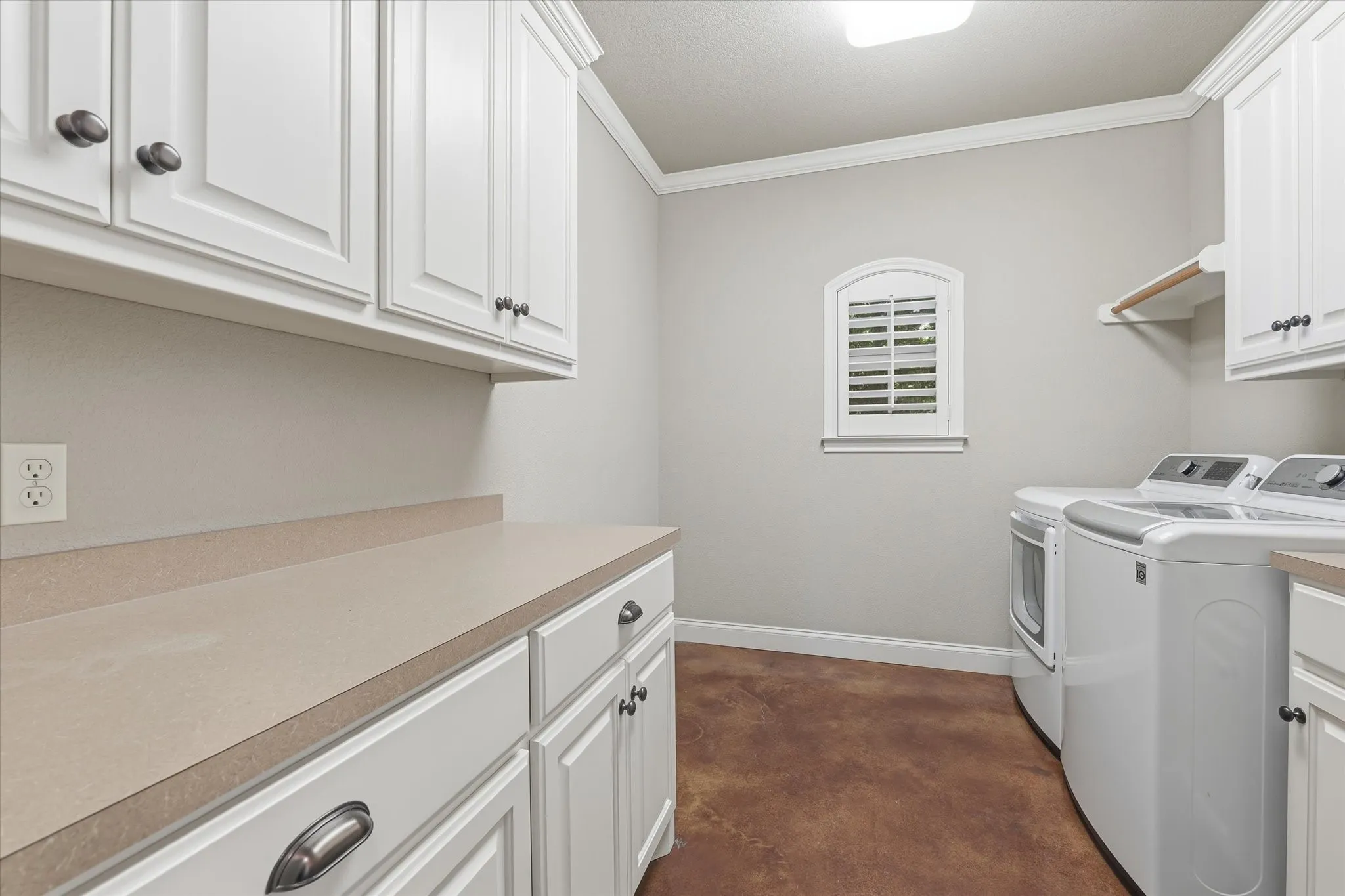 Laundry room featuring white cabinetry, a light-toned countertop, and a small arched window with plantation shutters