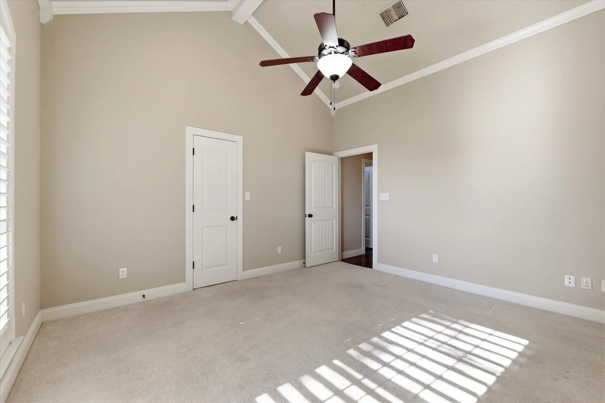 Carpeted room featuring a vaulted ceiling with exposed beams, an attached ceiling fan, and plantation shutters