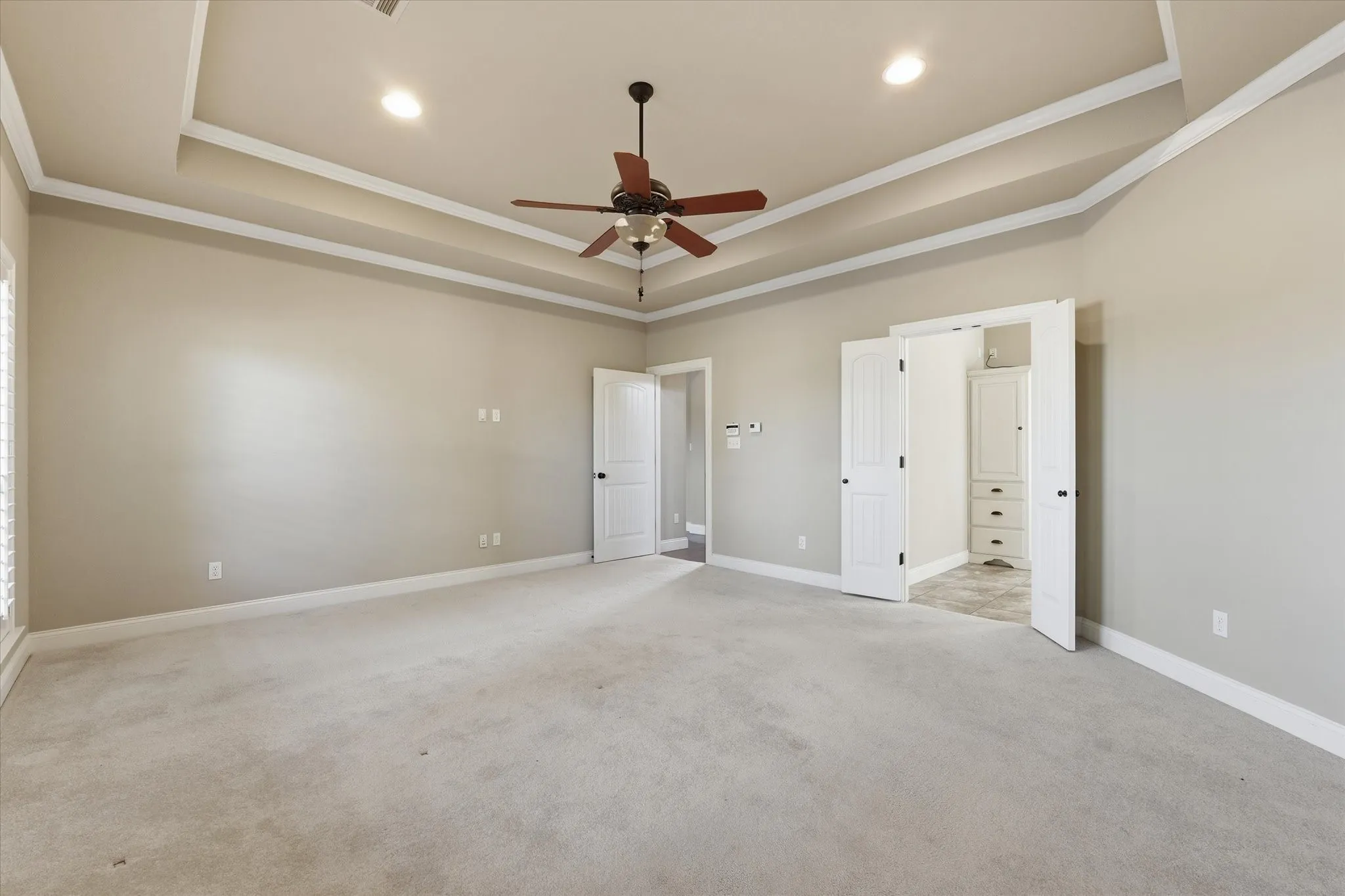 Spacious room featuring tray ceiling with recessed lighting, ceiling fan, neutral carpet, and white trim