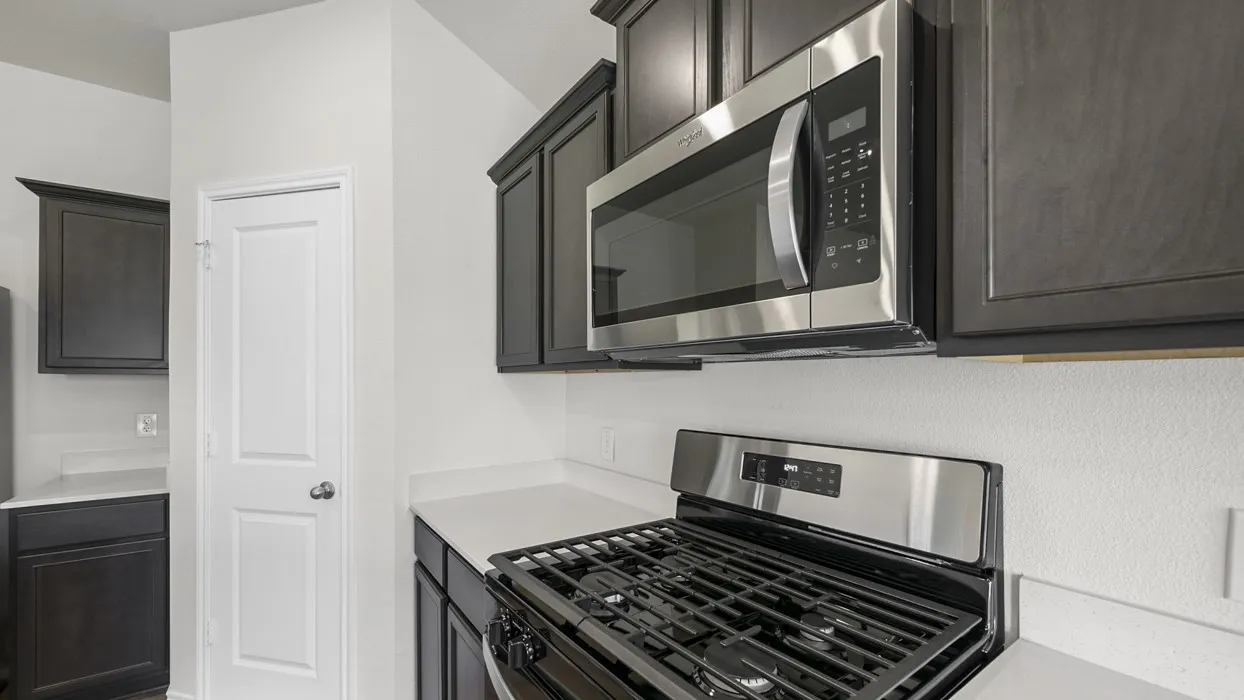Modern kitchen featuring dark wood-finish cabinetry, stainless steel appliances including a gas range and over-the-range microwave, and light-colored countertops