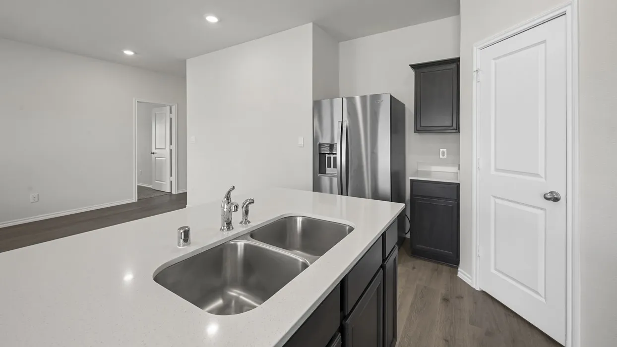 Kitchen island featuring a double basin stainless steel sink with a chrome faucet, light-toned countertop, and dark cabinetry