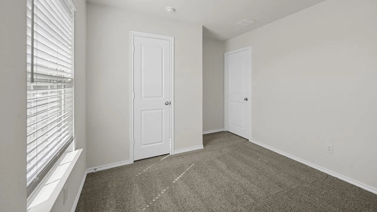 Neutral-toned room featuring a large window with horizontal blinds, light gray walls, and dark gray carpeting