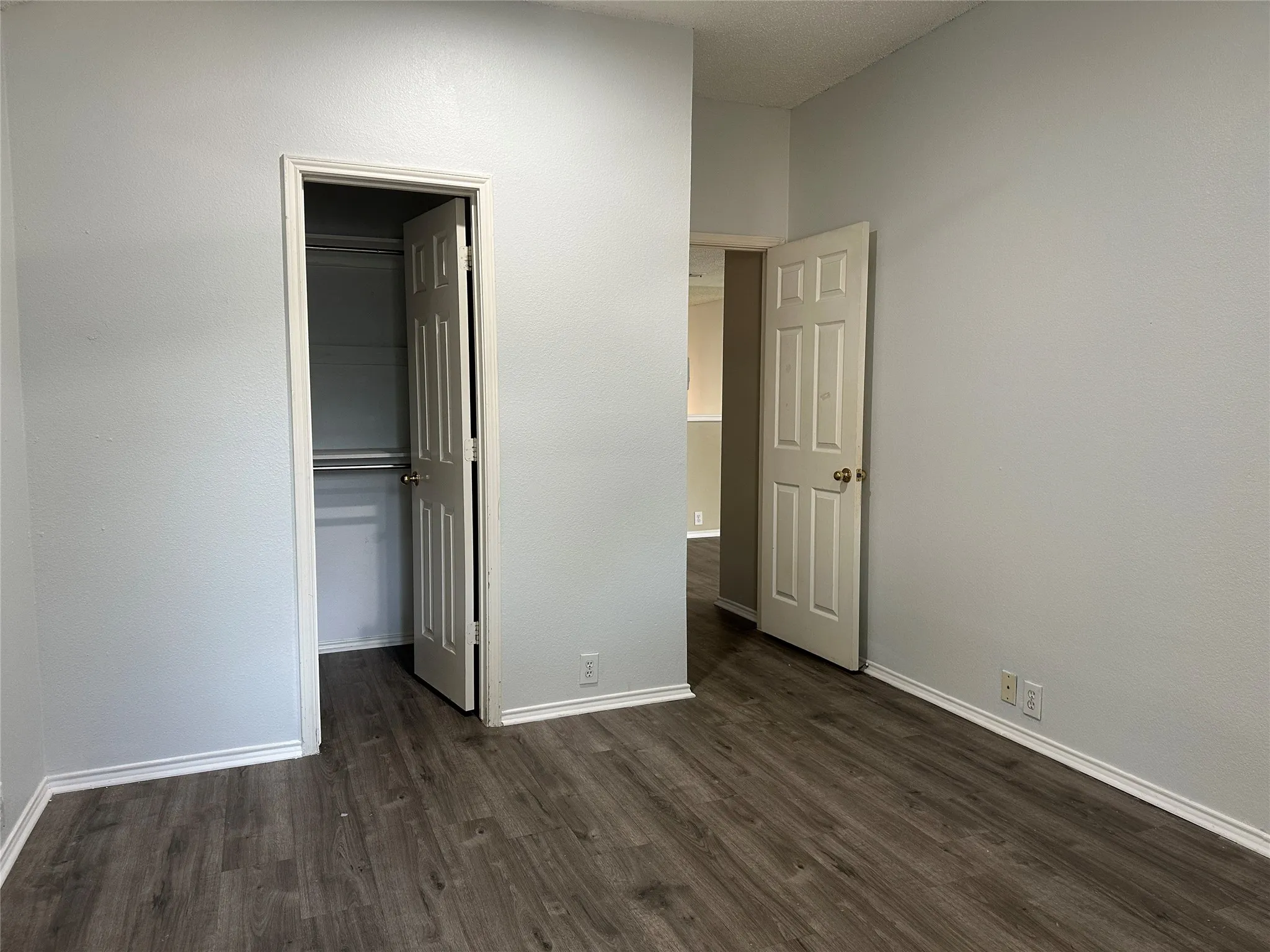 Room featuring wood-finish flooring, light grey walls, white baseboards, and white interior doors