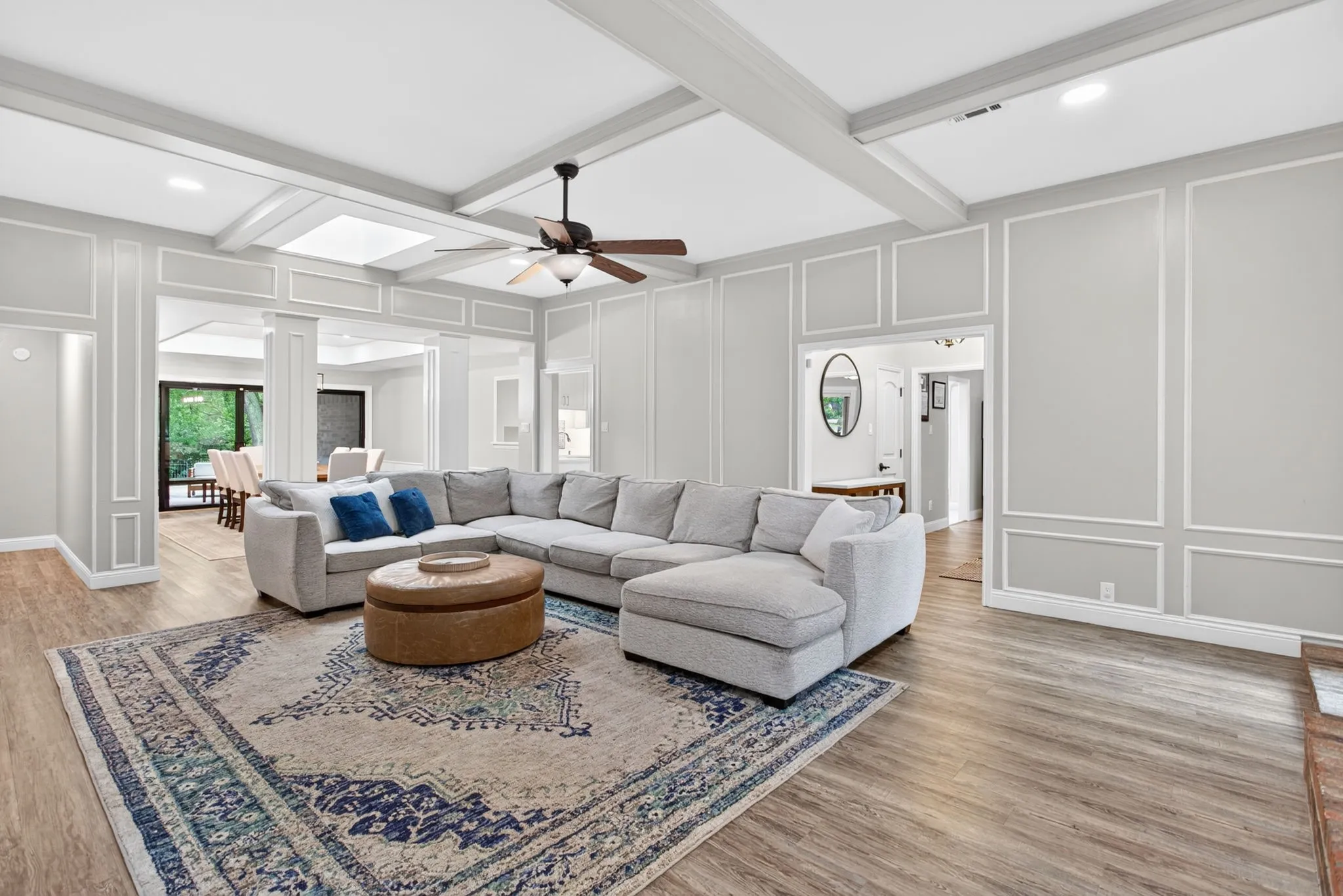 Spacious living area featuring wood-finish flooring, light gray walls with decorative trim, and a ceiling fan