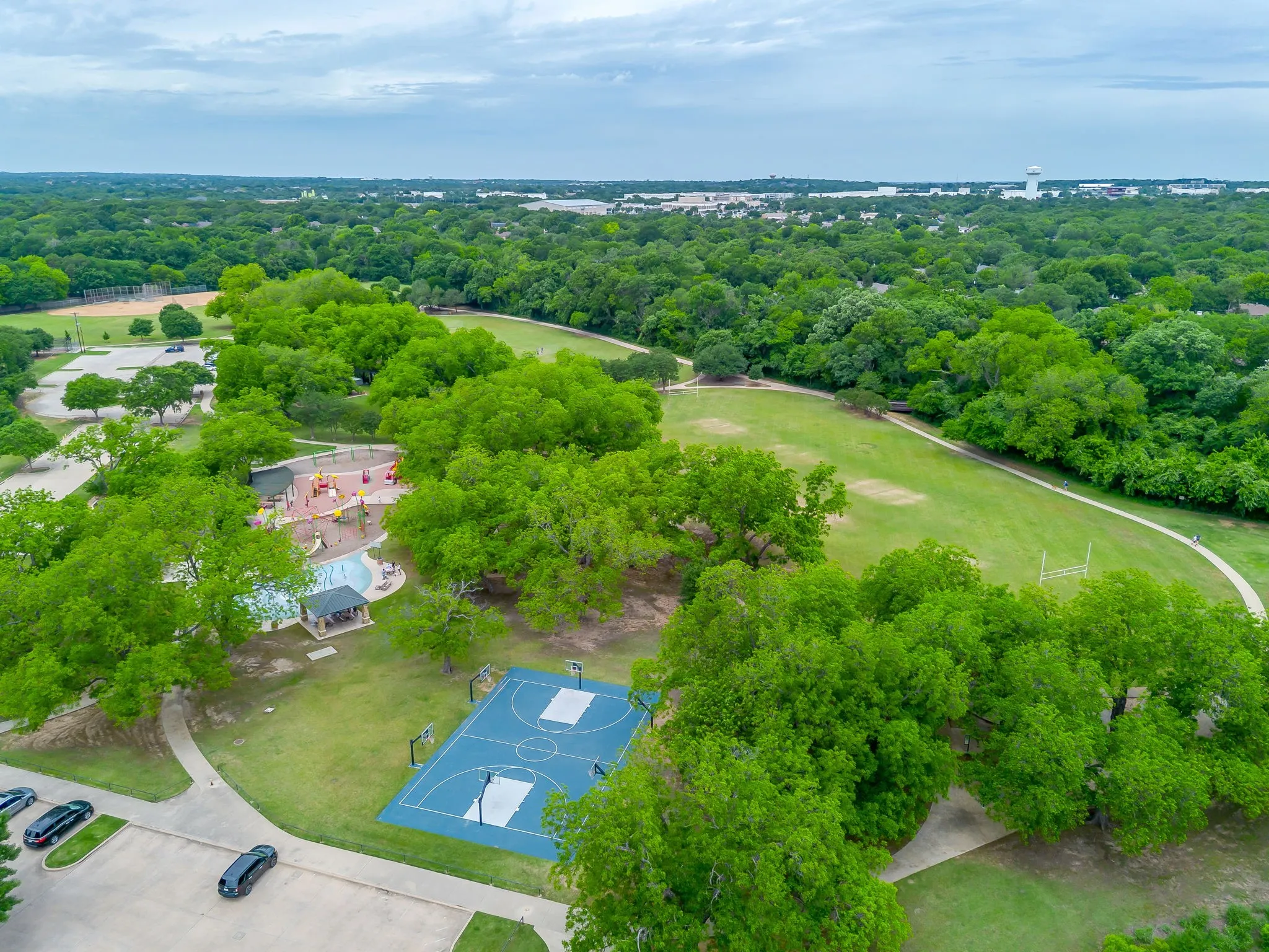 Parr Park amenities
Expansive green space featuring a blue basketball court, a recreational pool area, a playground, and extensive walking paths surrounded by mature trees
