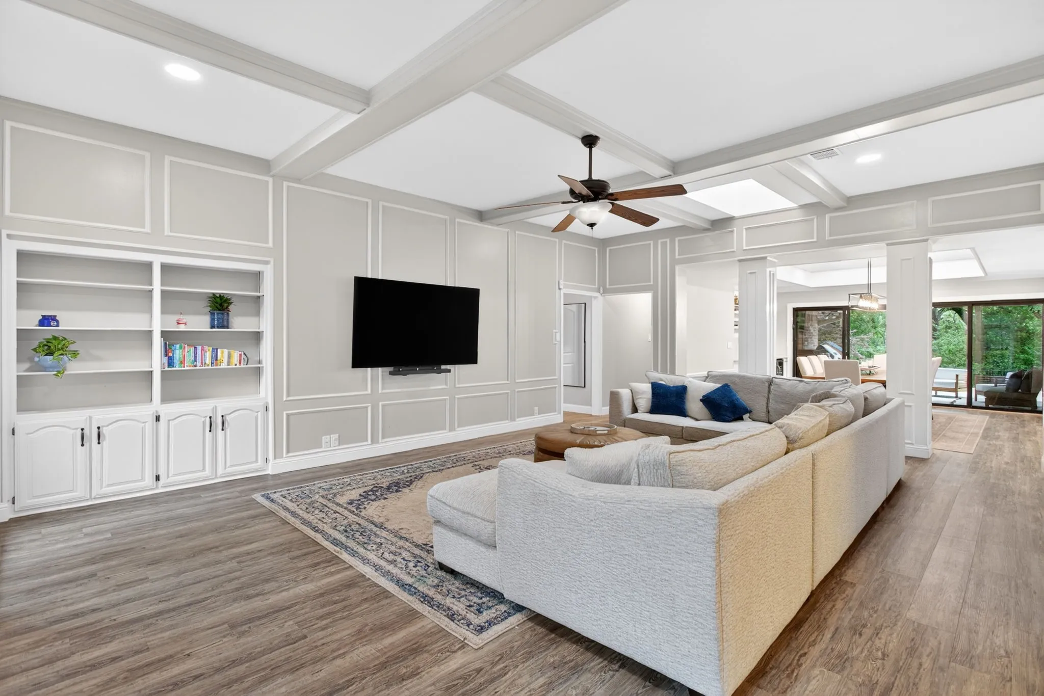 Spacious living area featuring wood-finish flooring, coffered ceilings, and decorative wall paneling