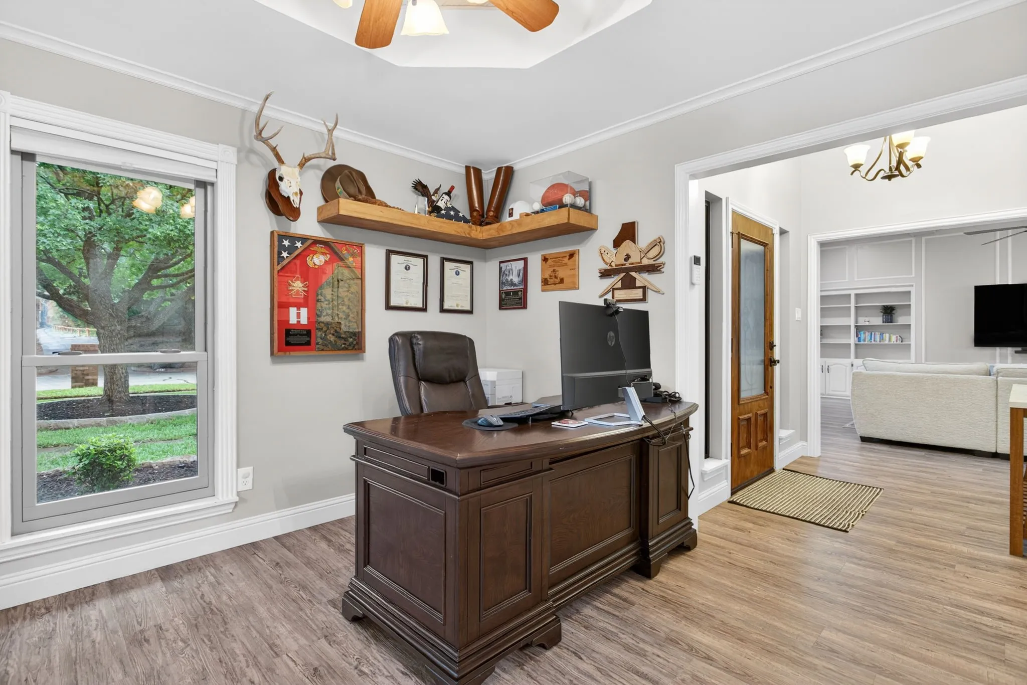 Office space featuring wood-finish flooring, a large window, crown molding, and a built-in corner shelf