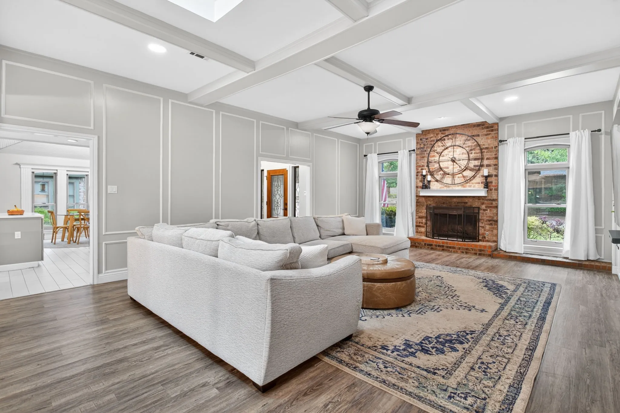 Spacious living area featuring exposed ceiling beams, wood-finish flooring, and light gray paneled walls