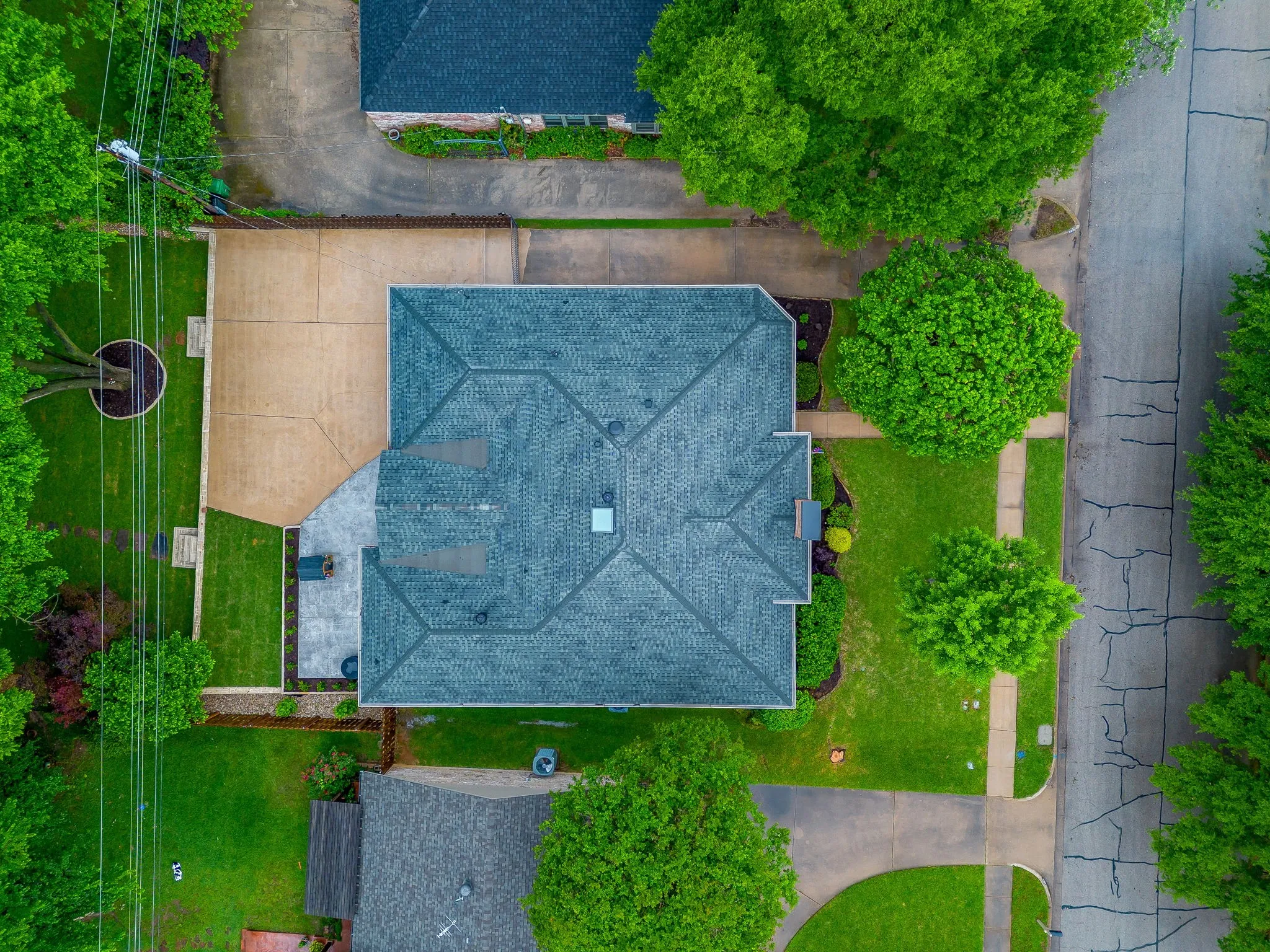 Property featuring a multi-gabled roof, expansive concrete driveway, and a stone patio