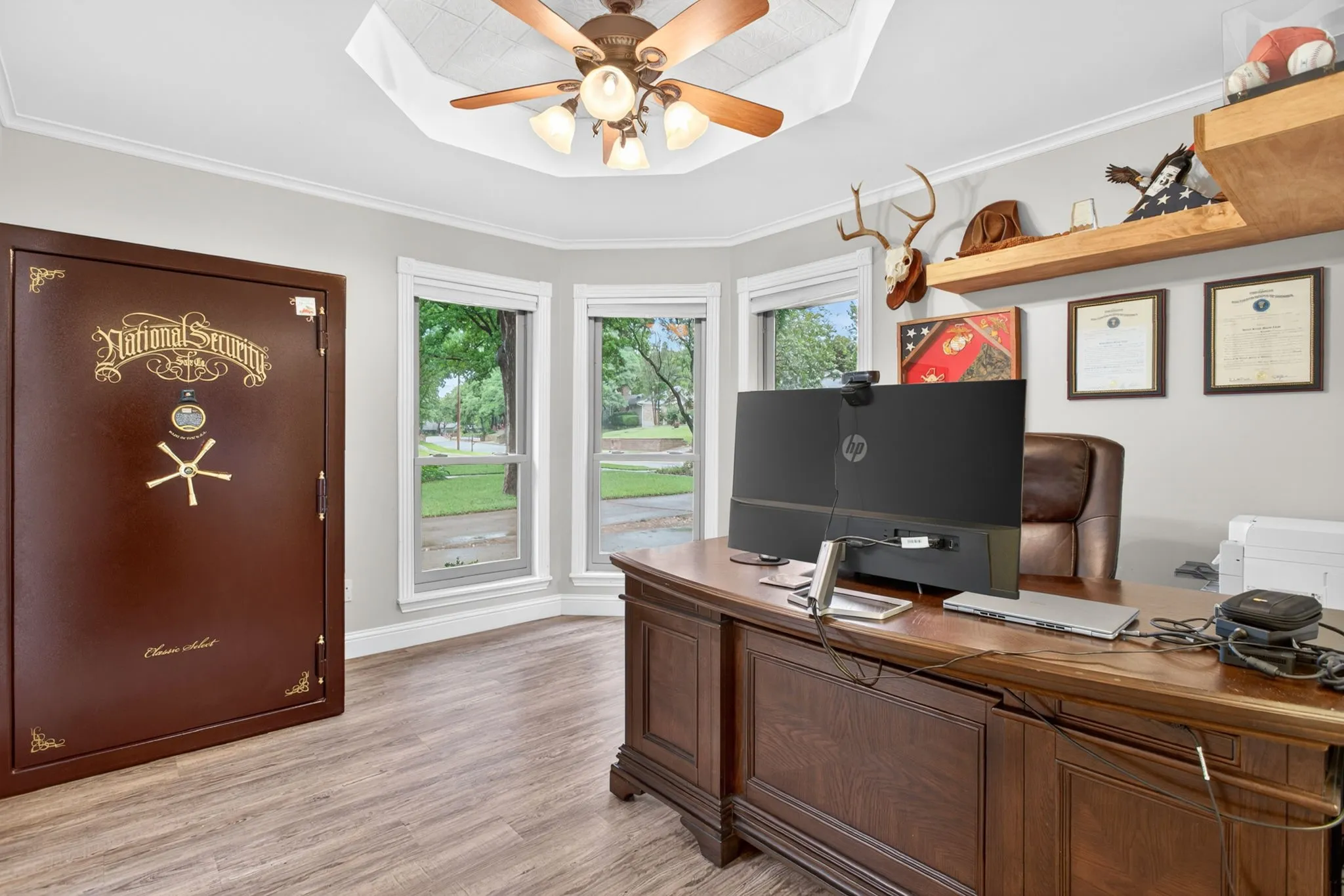 Secure room featuring a built-in safe door, bay windows, wood-finish flooring, a built-in ceiling fan with lighting, and crown molding