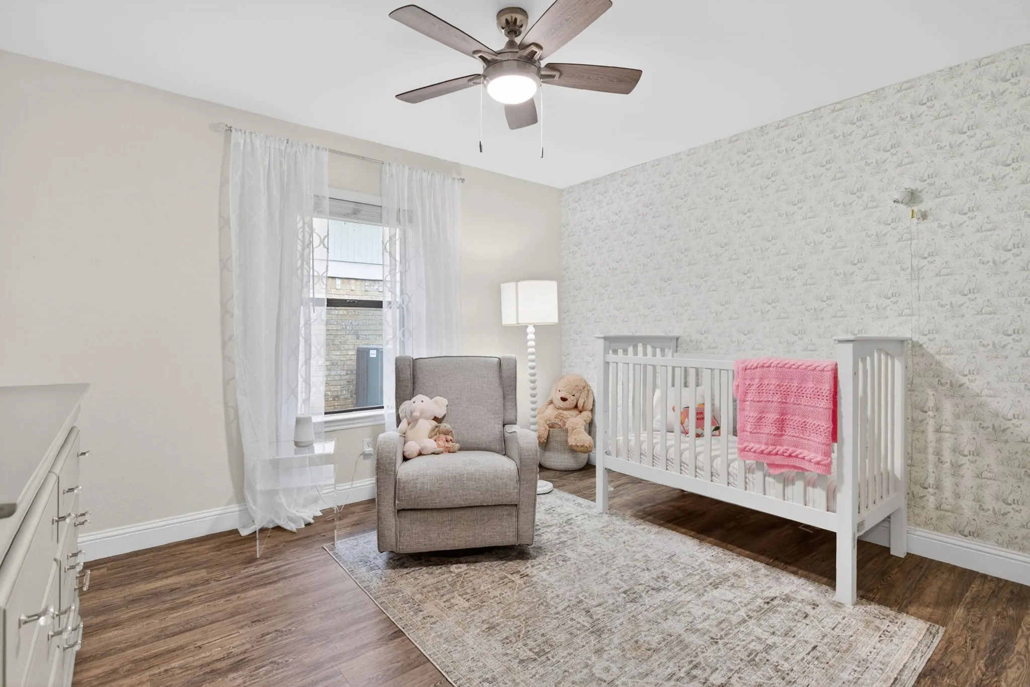Room featuring wood-finish flooring, a ceiling fan with integrated lighting, and a textured accent wall