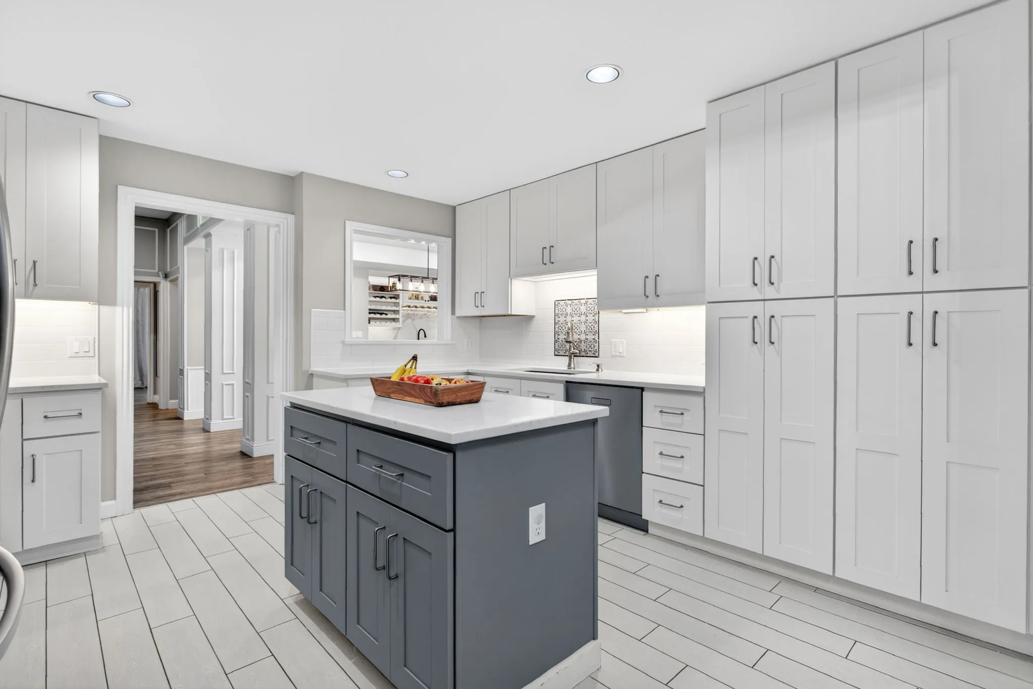 Modern kitchen featuring white shaker-style cabinetry, a contrasting grey island with storage, light-toned plank flooring, stainless steel appliances, and recessed lighting
