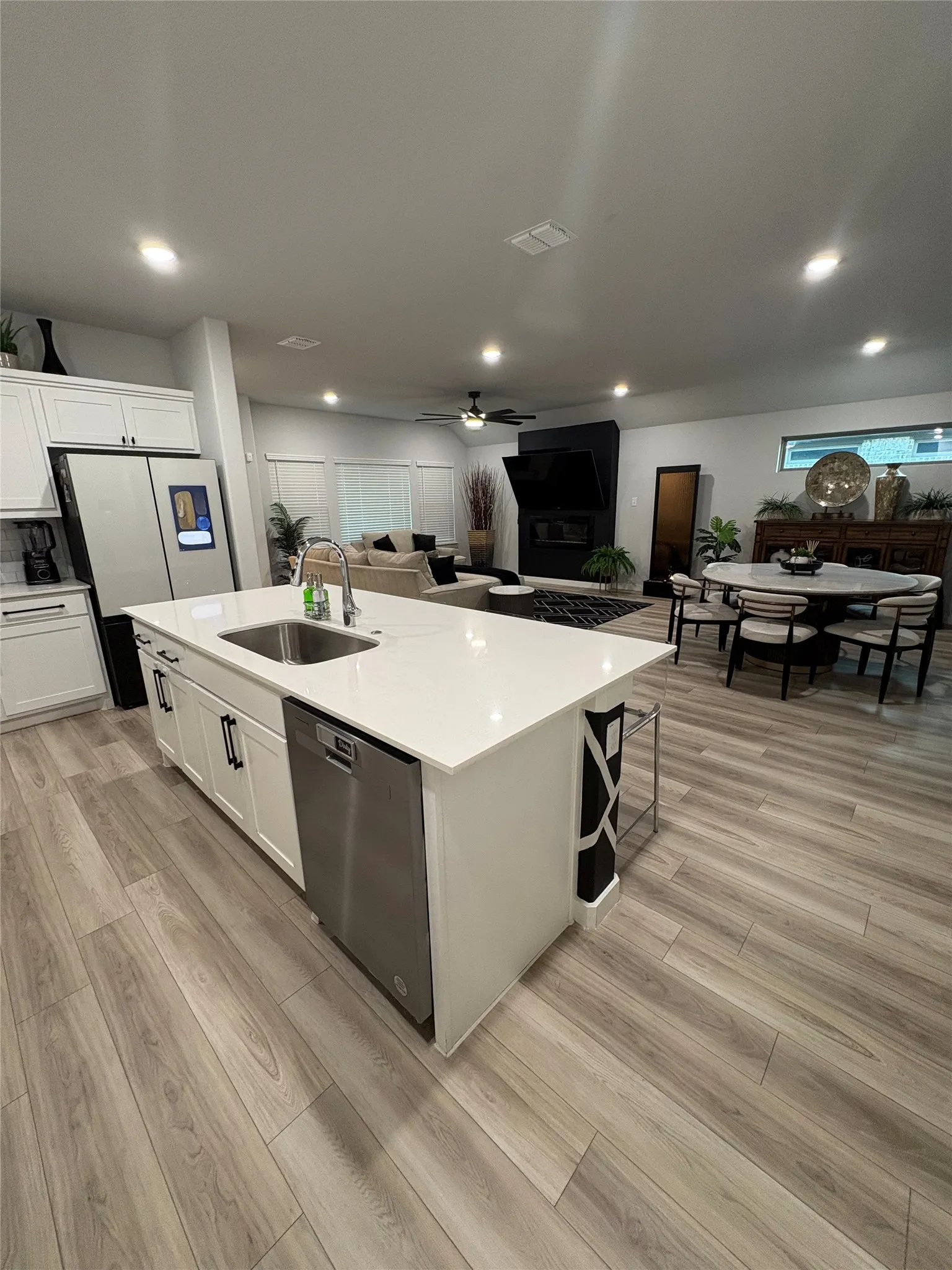Open-concept living space with wood-finish flooring, recessed lighting, and a kitchen island featuring a stainless steel sink and dishwasher
