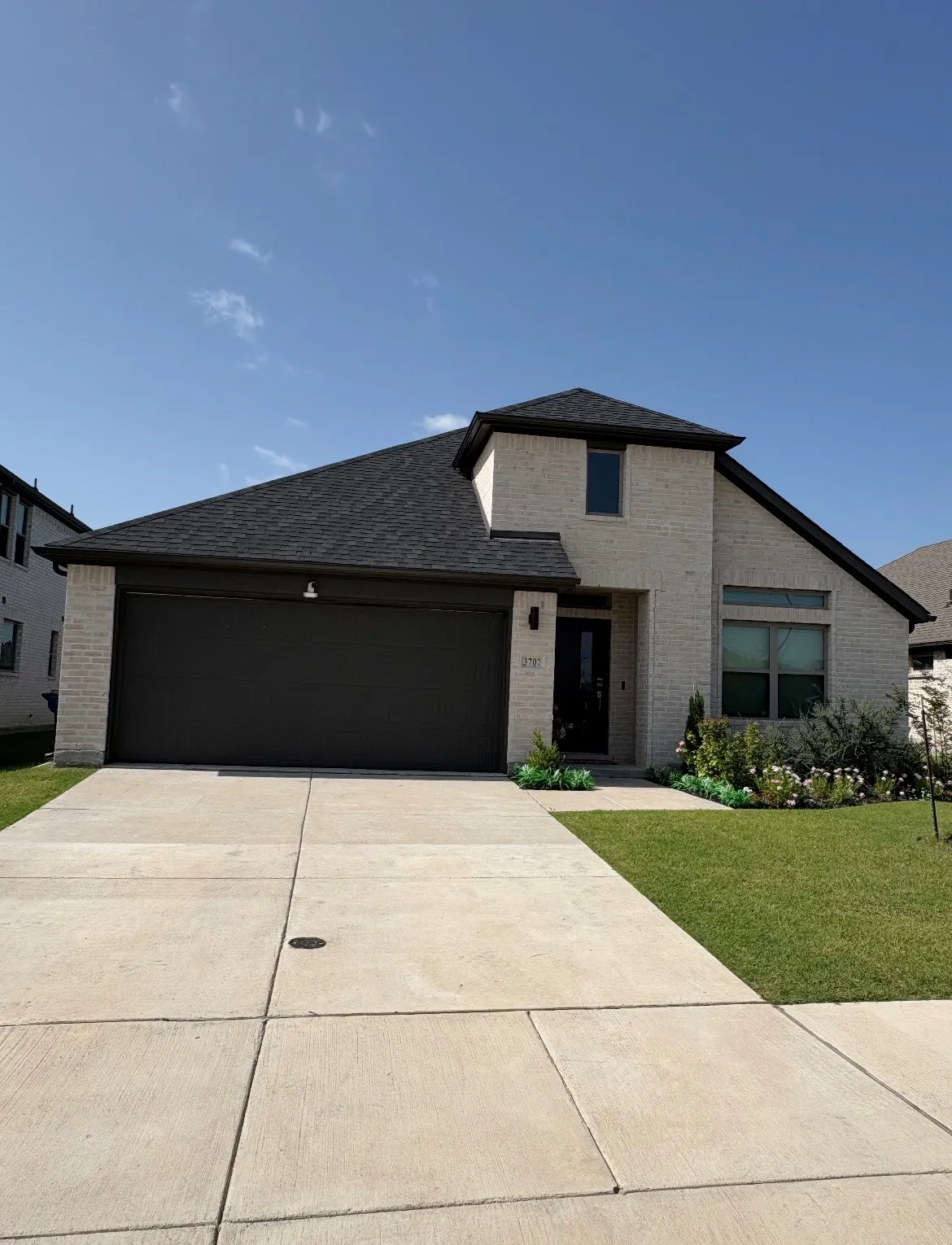 Modern brick and stone exterior with a two-car garage featuring a dark finish door, complemented by a wide concrete driveway and manicured lawn
