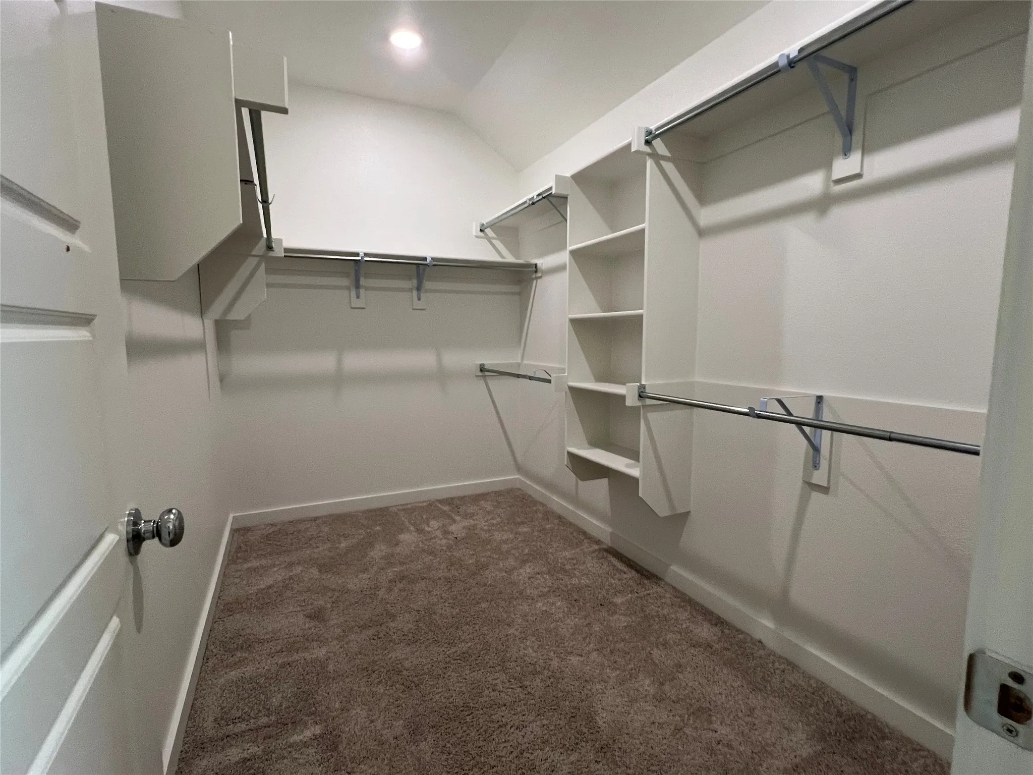 Spacious walk-in closet featuring multiple built-in shelving units, dual clothing rods with chrome hardware, and soft-close rod systems