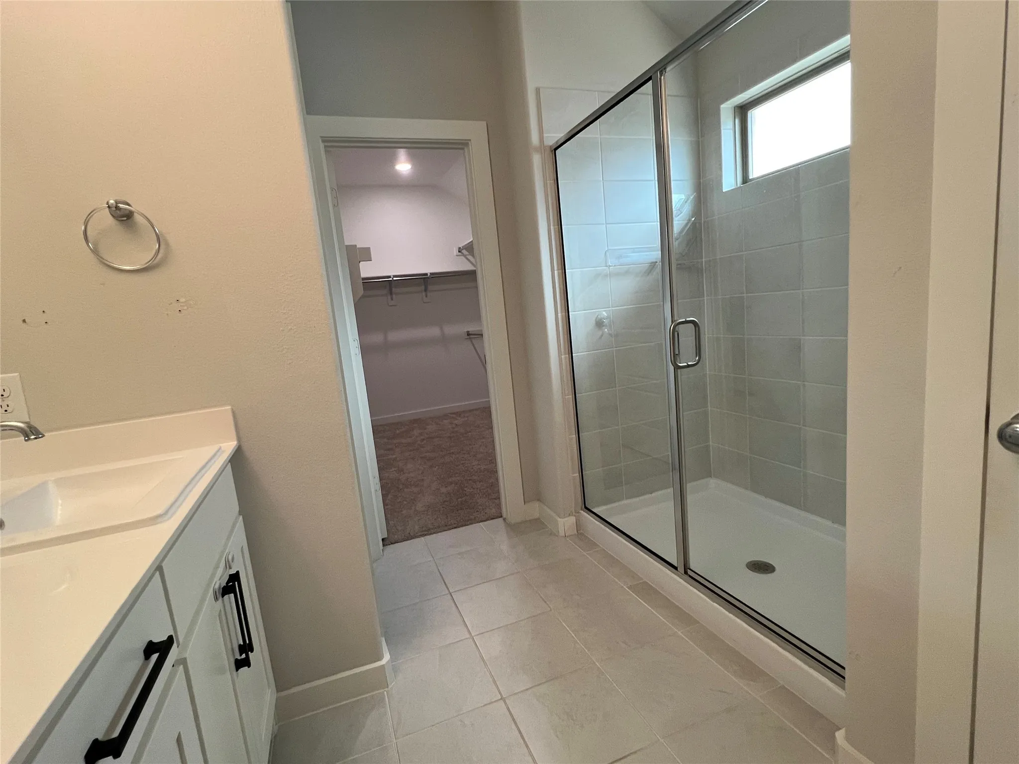 Primary Bathroom featuring a vanity with white cabinetry and countertop, tile flooring, and a frameless glass-enclosed shower with tile surround and chrome hardware