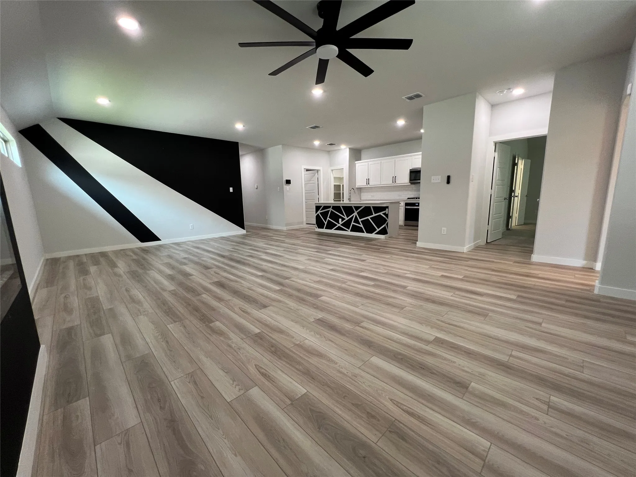 Spacious open-concept living area featuring wide-plank wood-finish flooring throughout, recessed ceiling lighting, and a modern ceiling fan