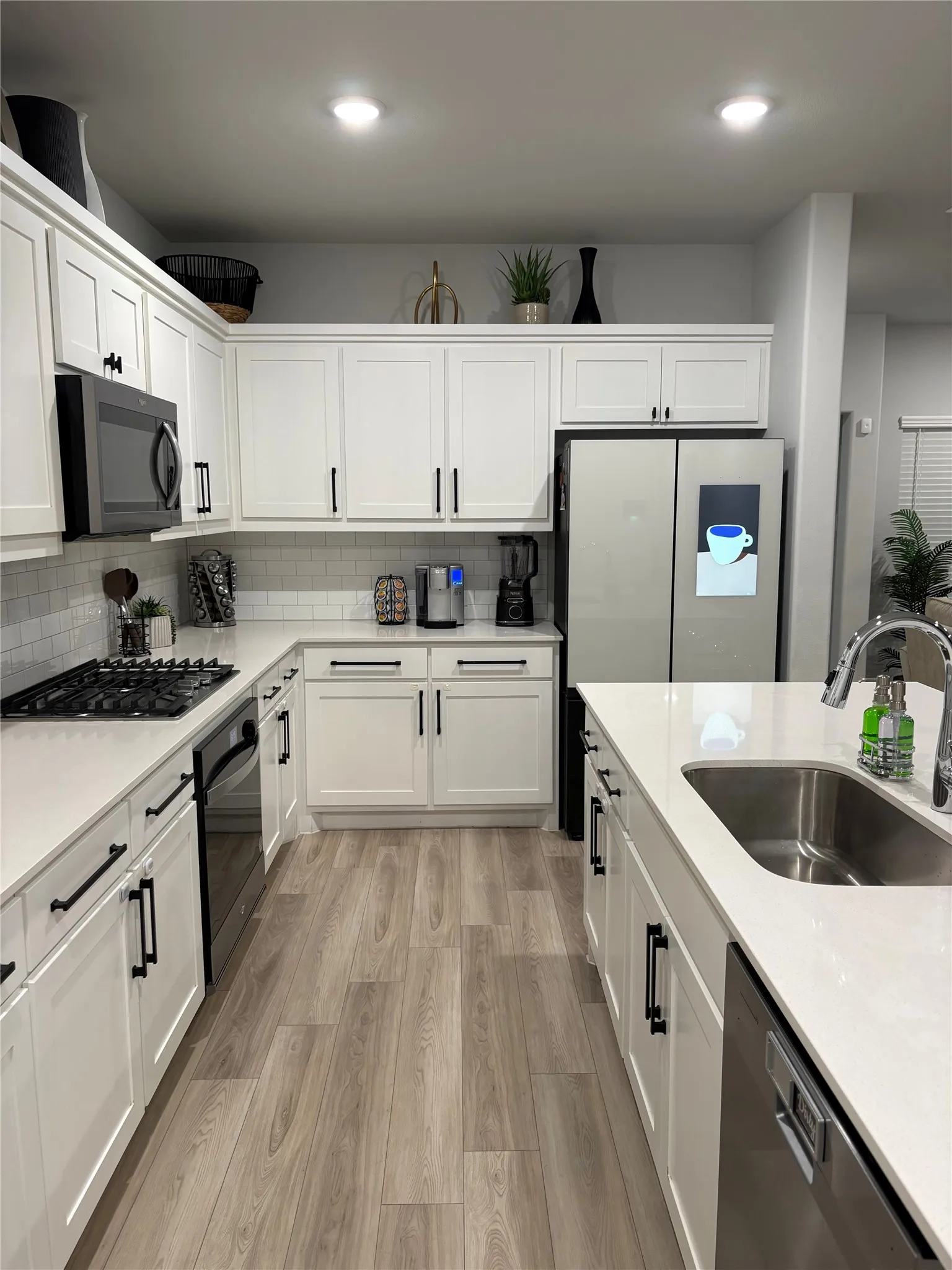 Modern kitchen featuring white shaker-style cabinetry with black hardware, quartz countertops, and a large waterfall-edge island
