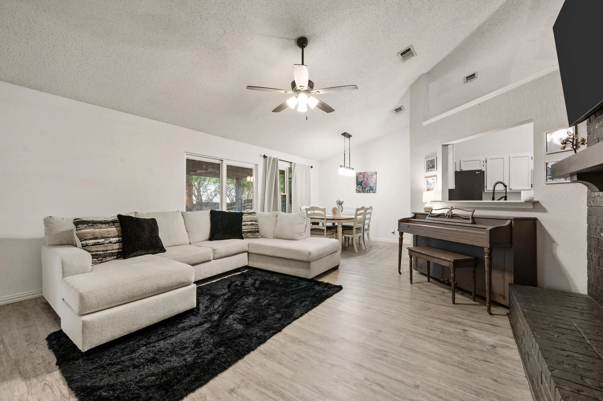 Vaulted ceiling great room featuring wood-finish flooring, a ceiling fan with integrated lighting, and a pass-through opening to a kitchen area