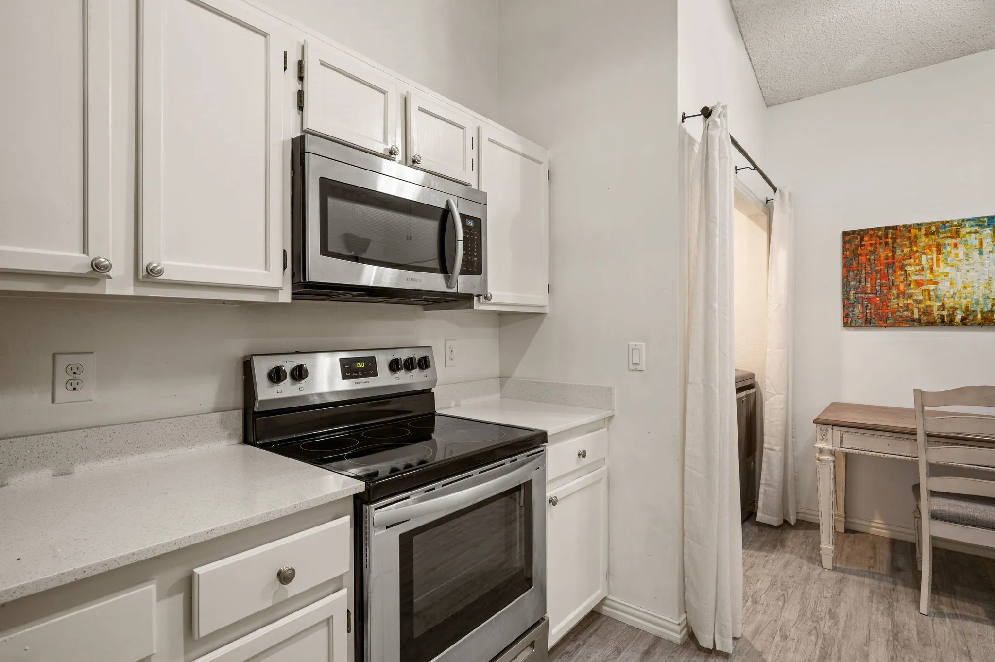 Modern kitchen featuring white cabinetry, light-colored countertops, stainless steel appliances including an oven range and microwave, and wood-finish flooring