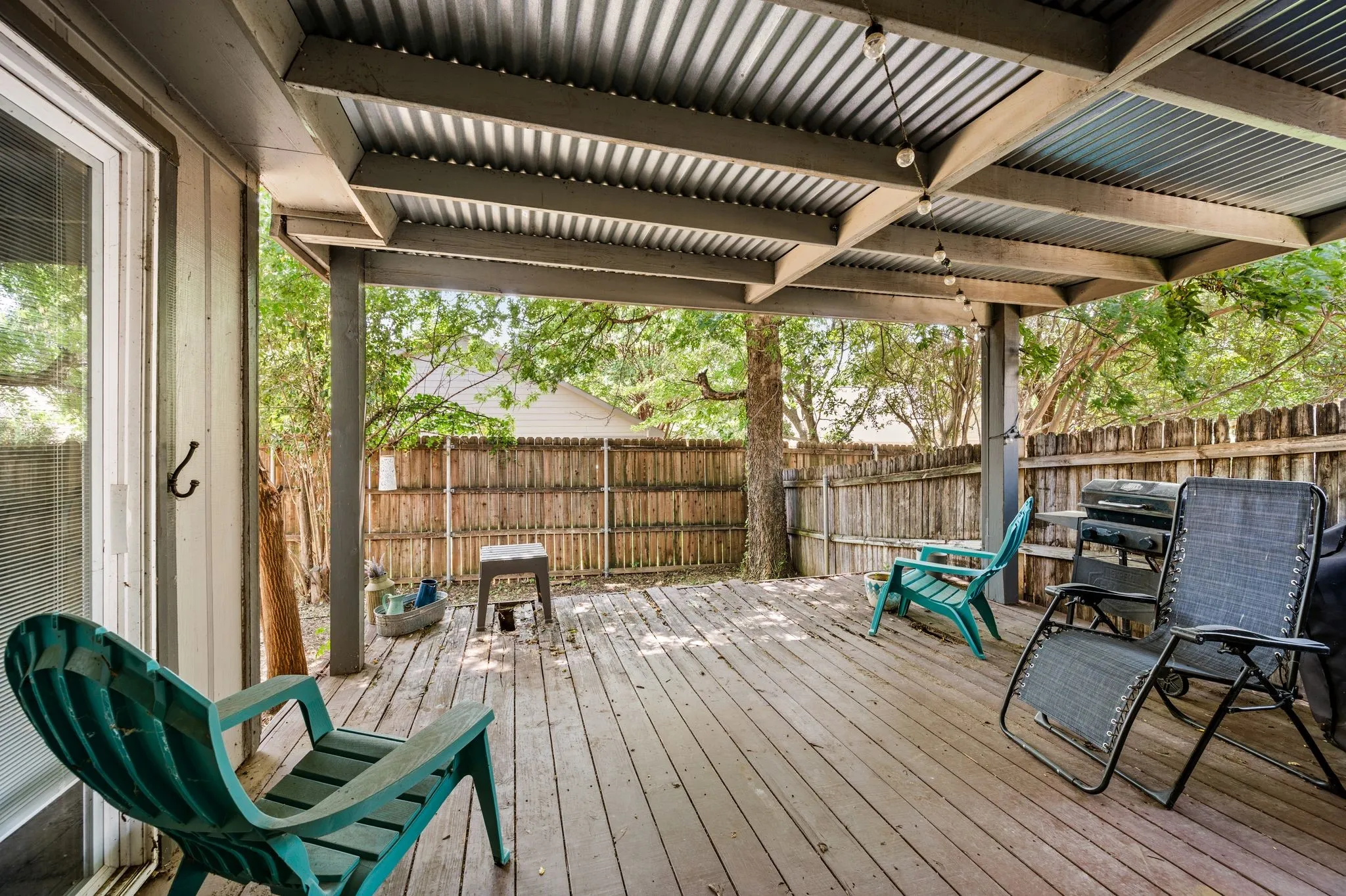 Expansive wood-finish deck with a corrugated metal patio cover and string lighting