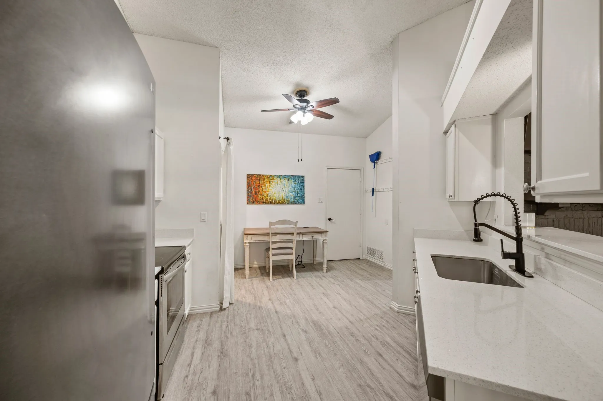 Kitchen featuring light wood-finish flooring, white cabinetry, integrated stainless steel sink with a matte black faucet, and white countertops