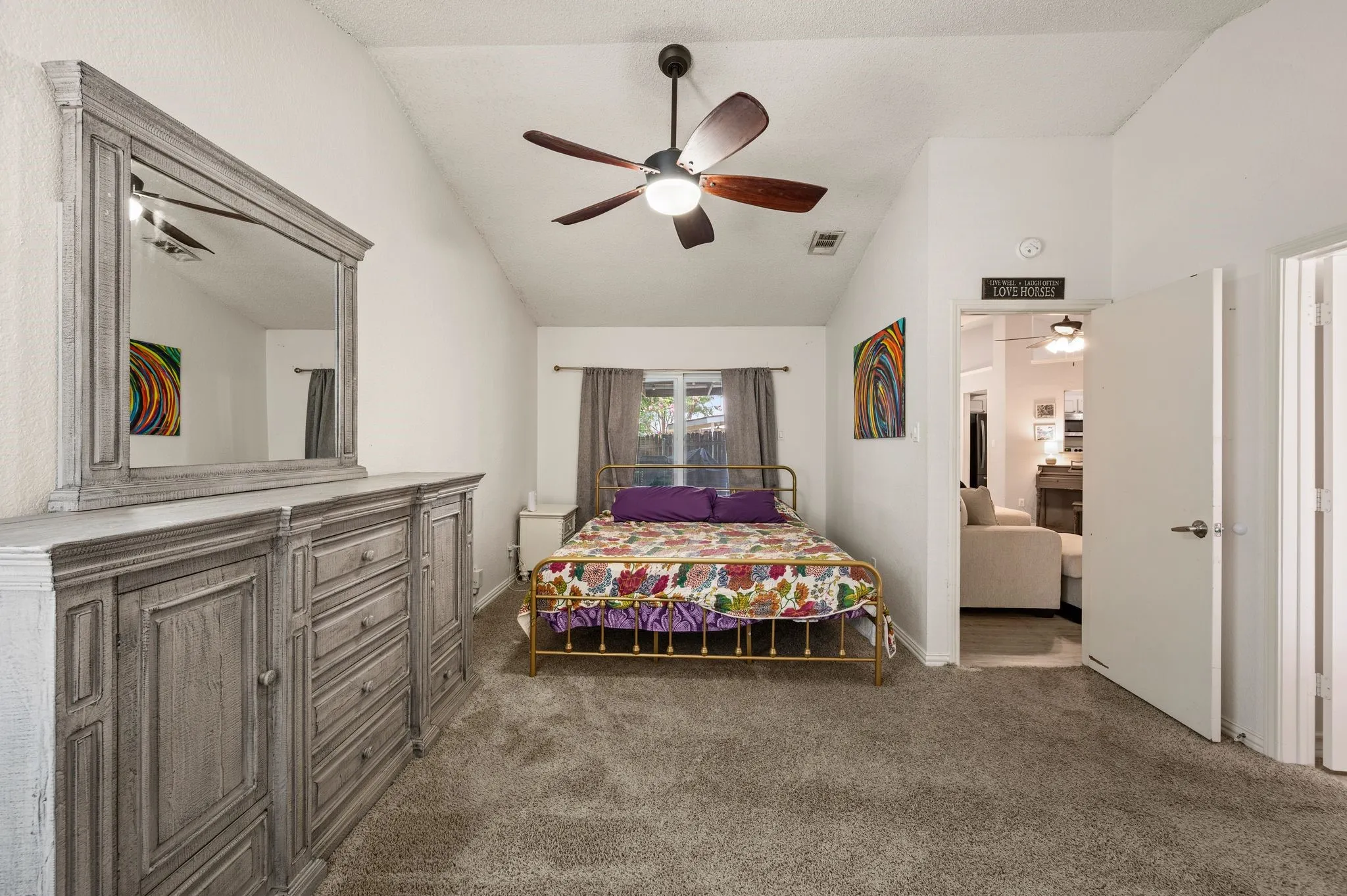 Vaulted ceiling bedroom featuring plush carpeting, a ceiling fan with light fixture, and a window with drapes