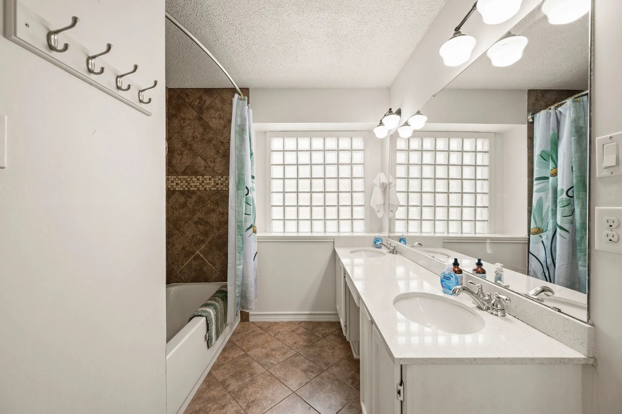 Bathroom featuring a double vanity with white countertops and integrated sinks, a full-width mirror, and a bathtub with brown tile surround