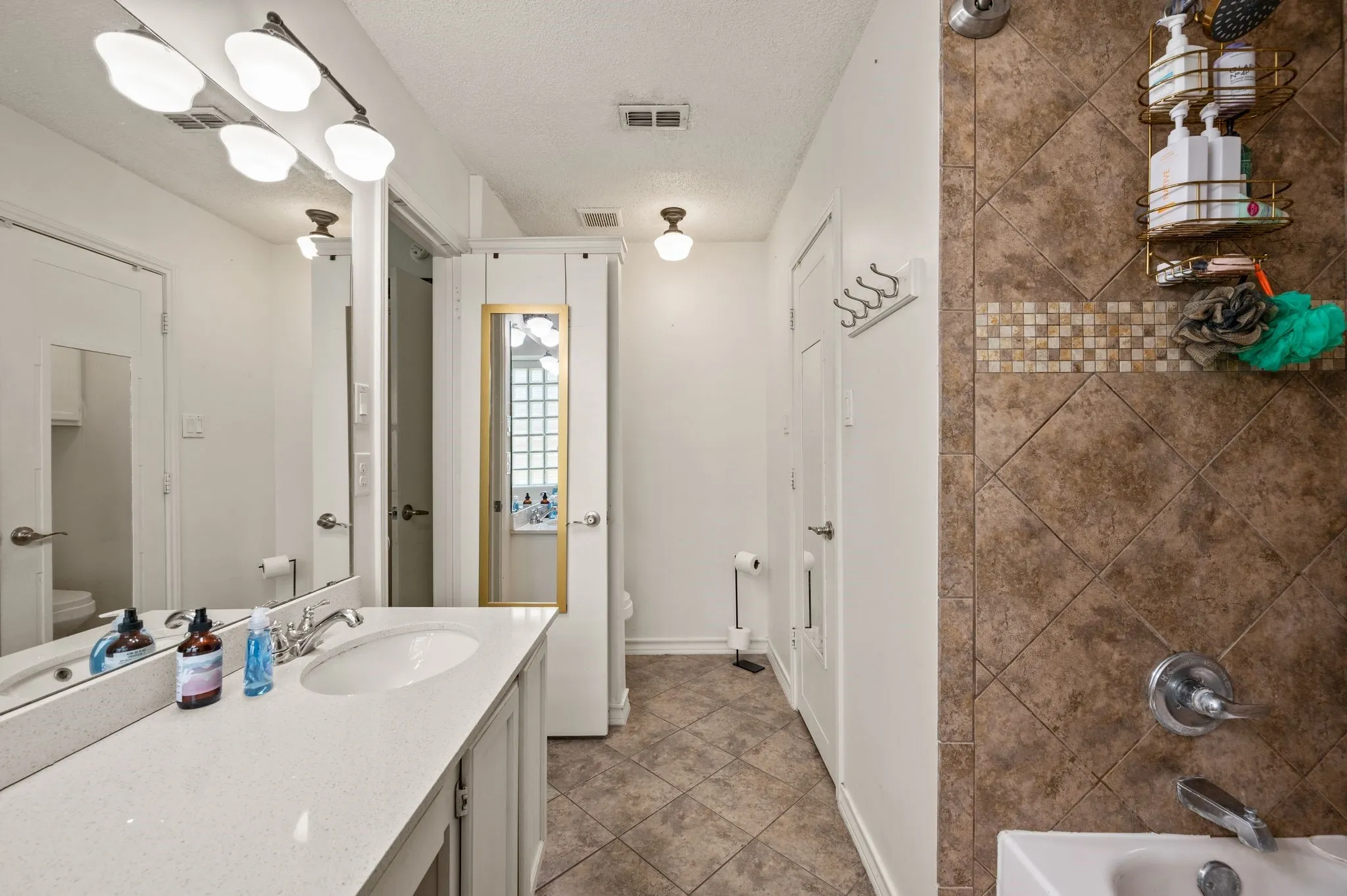 Bathroom featuring an extended vanity with a solid surface countertop and undermount sink, a large wall mirror, and a three-light fixture