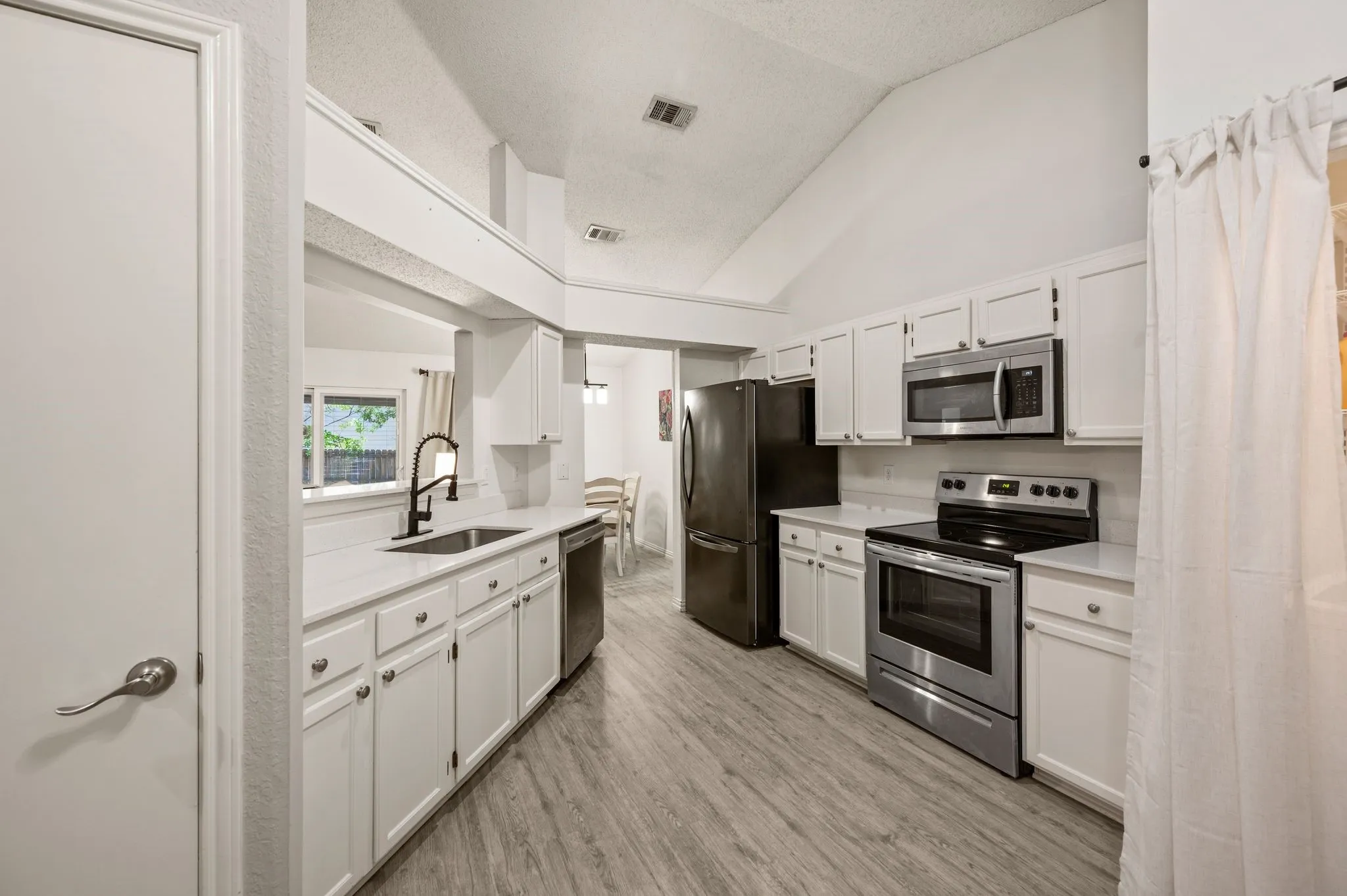 Kitchen featuring vaulted ceilings, white cabinetry, light-toned countertops, wood-finish flooring, and stainless steel appliances