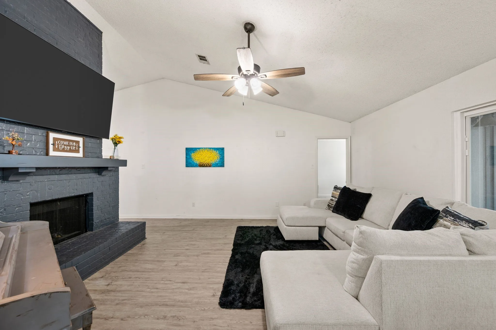 Living area featuring a painted brick fireplace with a mantel, vaulted ceilings, and wood-finish flooring