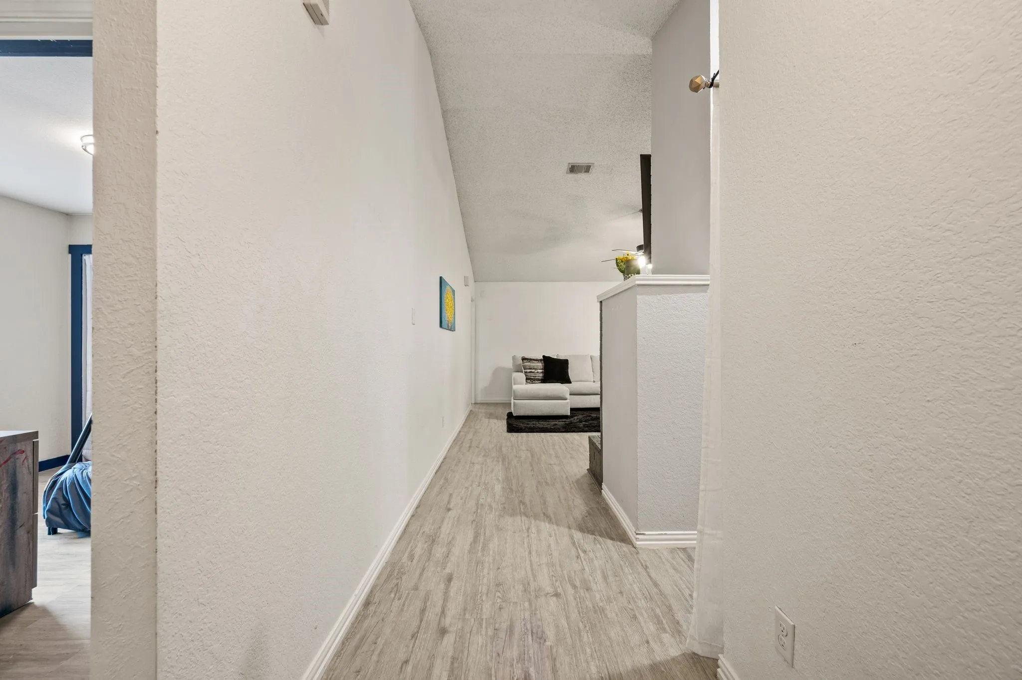 Hallway featuring wood-finish flooring, textured walls, and a partial view into an additional room