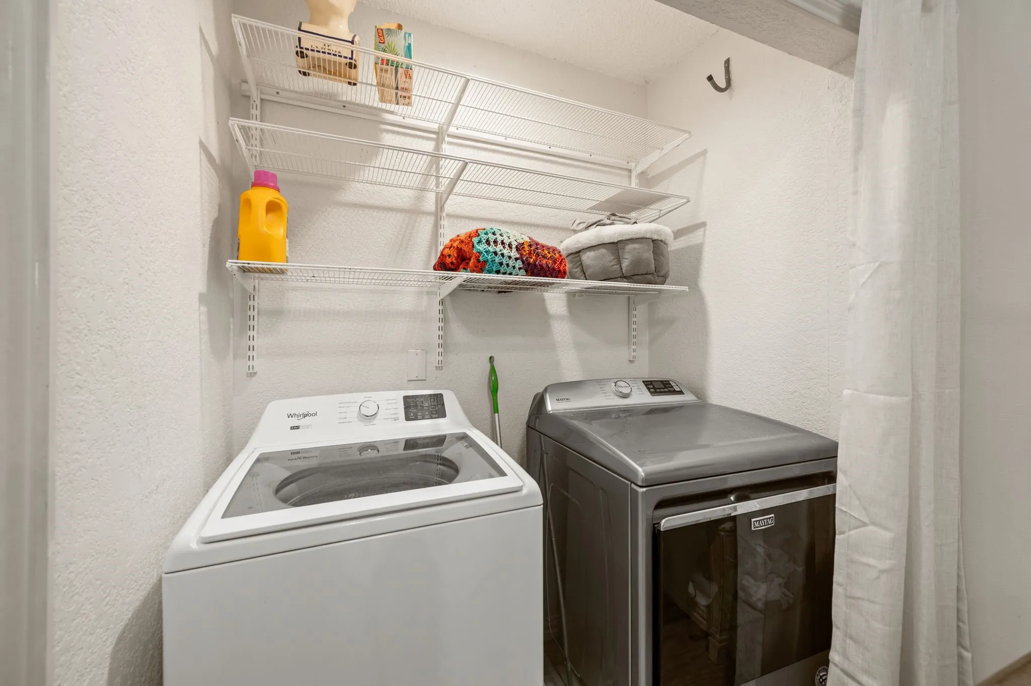 Dedicated laundry area featuring white textured walls, integrated wire shelving, and a hanging hook
