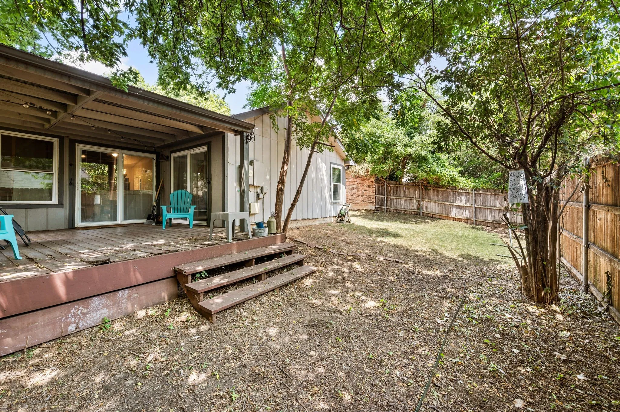 Spacious backyard featuring a wood deck, sliding glass doors, a slatted patio cover, a partial privacy fence, and mature trees