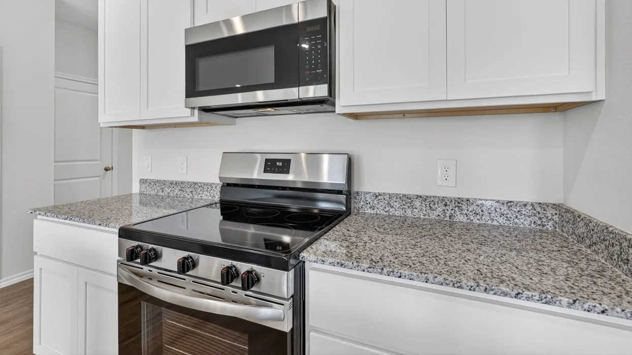 Modern kitchen featuring white shaker cabinetry, speckled countertops, stainless steel appliances, and wood-finish flooring