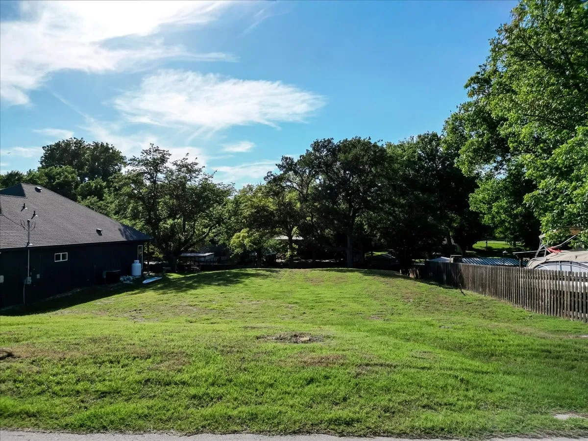 Expansive green lot with established perimeter fencing, mature trees, and a clear blue sky
