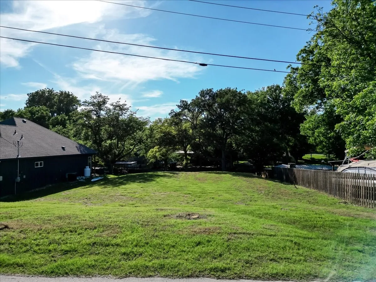 Expansive lot featuring a large grassy area, mature trees bordering the property, and a wooden privacy fence along one side