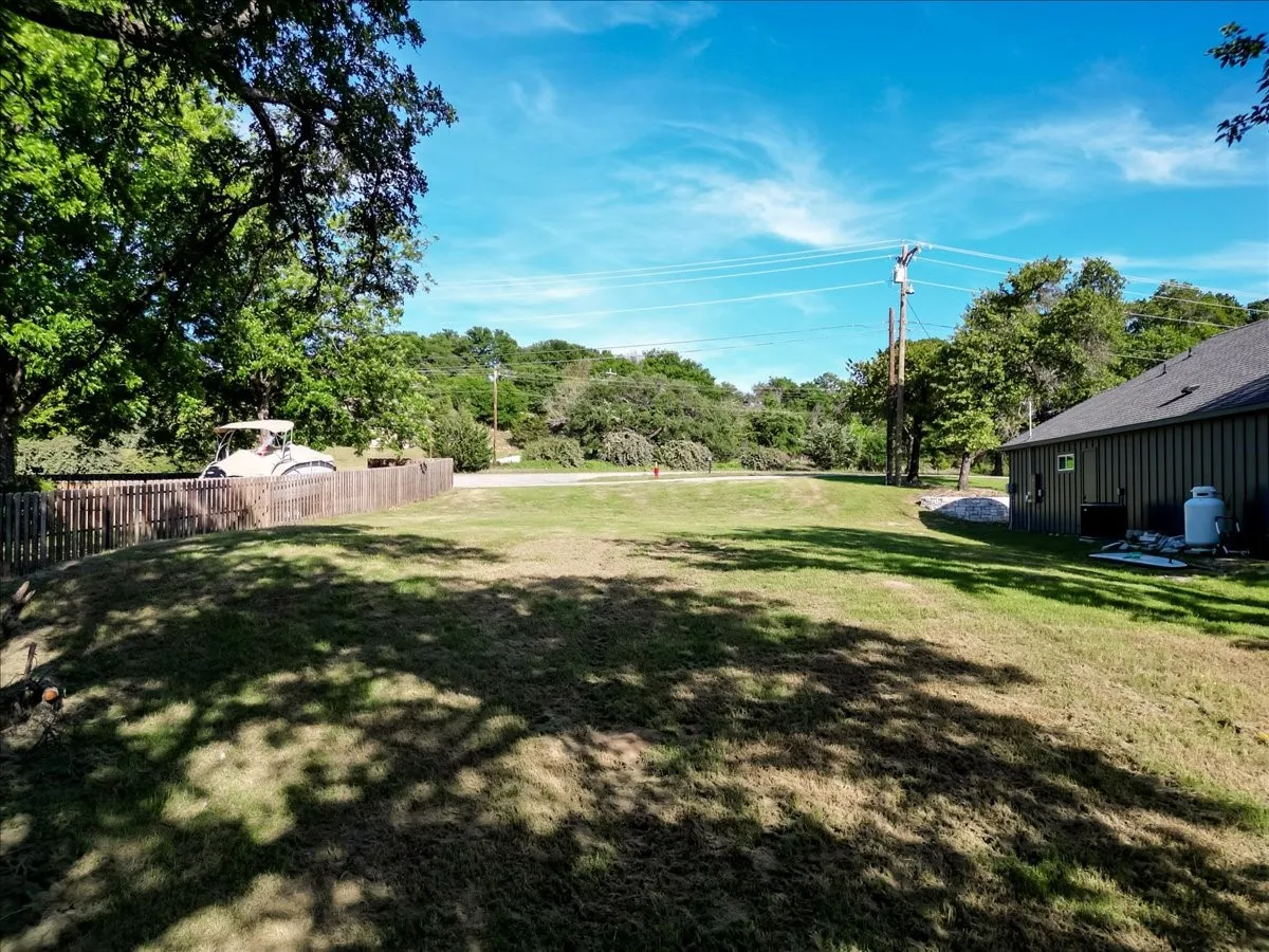 Expansive lawn area featuring a wooden privacy fence, mature trees, and a visible utility structure