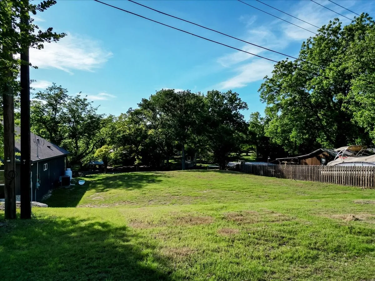 Expansive grassy yard with mature trees and partial fencing