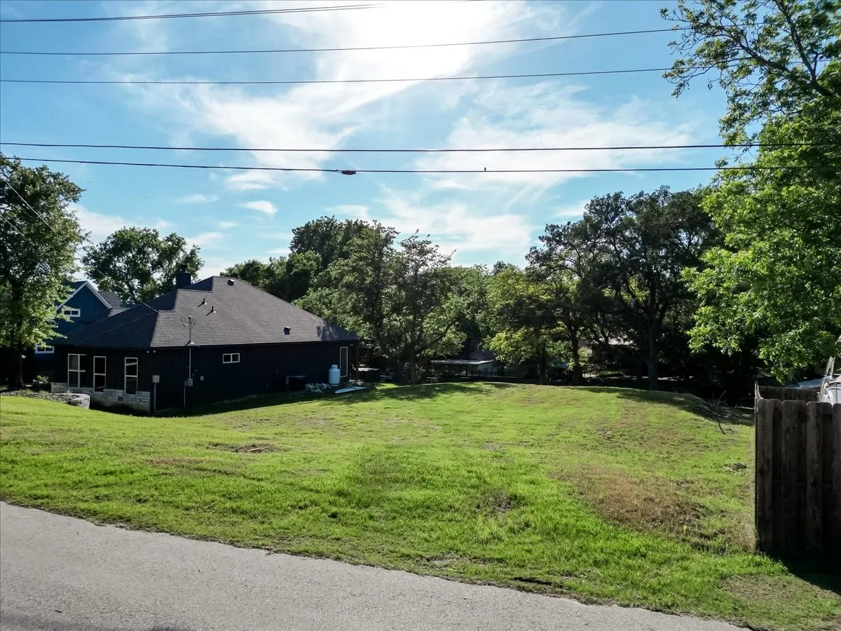 Expansive grassy lot featuring mature trees and a partial wood fence